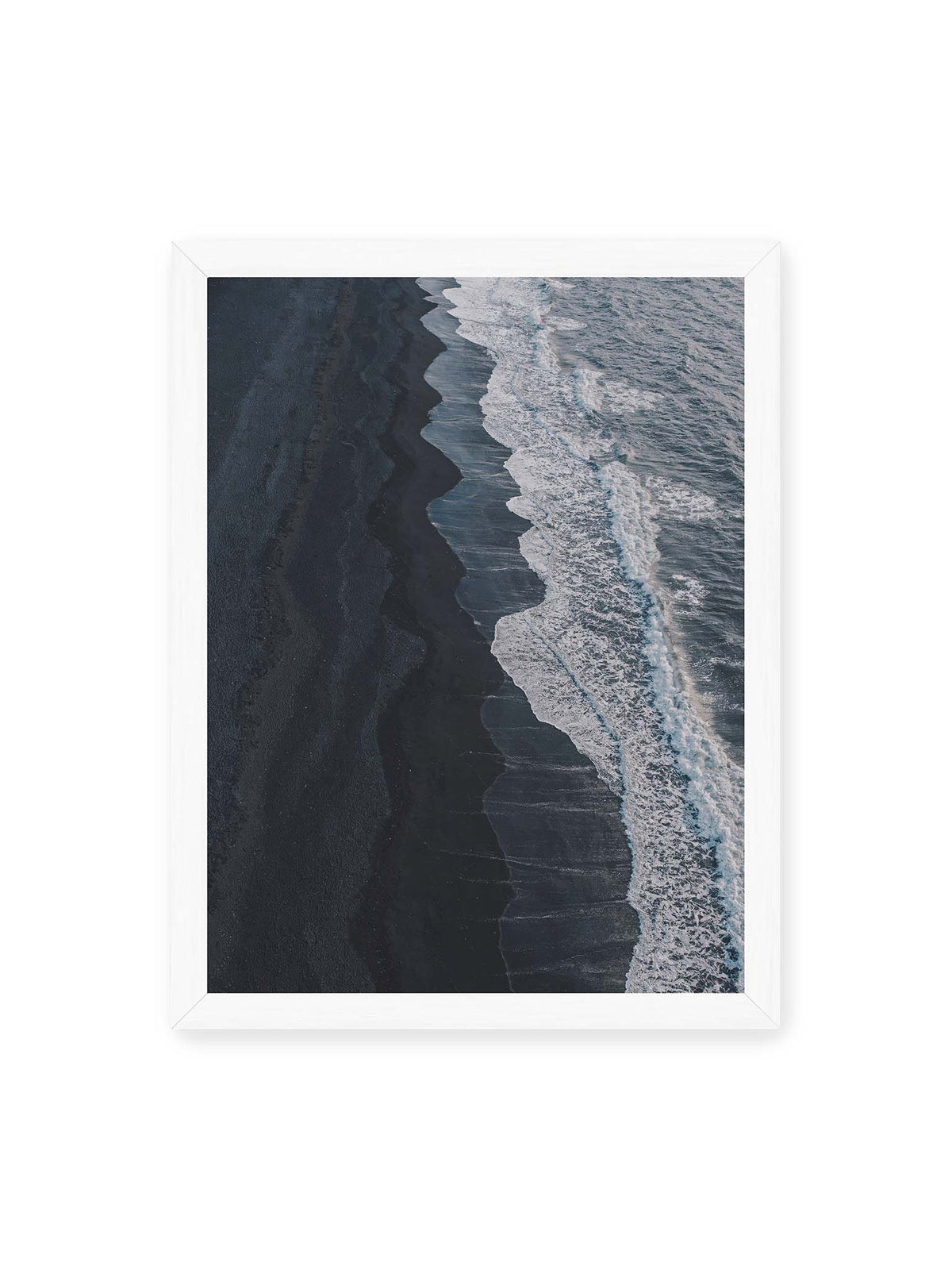 30x40 cm, weißer Rahmen – Dunkler Strand aus erhöhter Perspektive mit weißer Brandung und blau-grauem Meer entlang einer geschwungenen Küstenlinie.