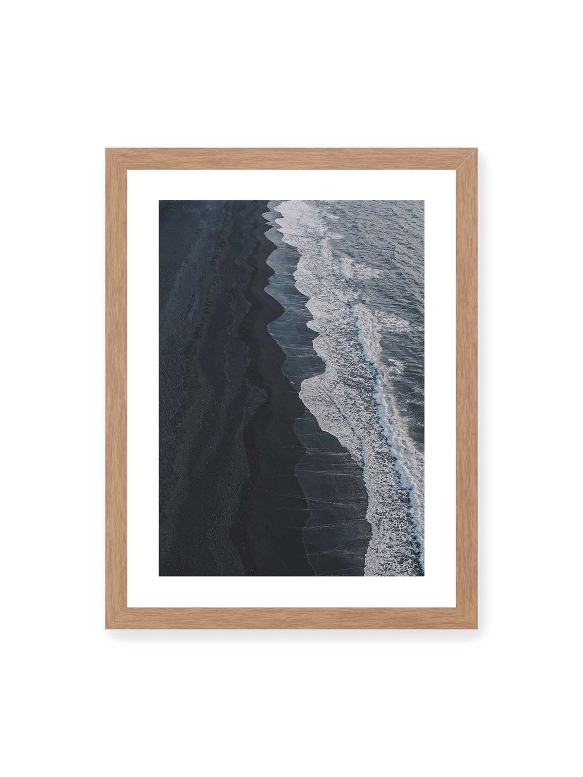 30x40 cm, weißer Galerie-Rand, Eichenrahmen – Dunkler Strand aus erhöhter Perspektive mit weißer Brandung und blau-grauem Meer entlang einer geschwungenen Küstenlinie.