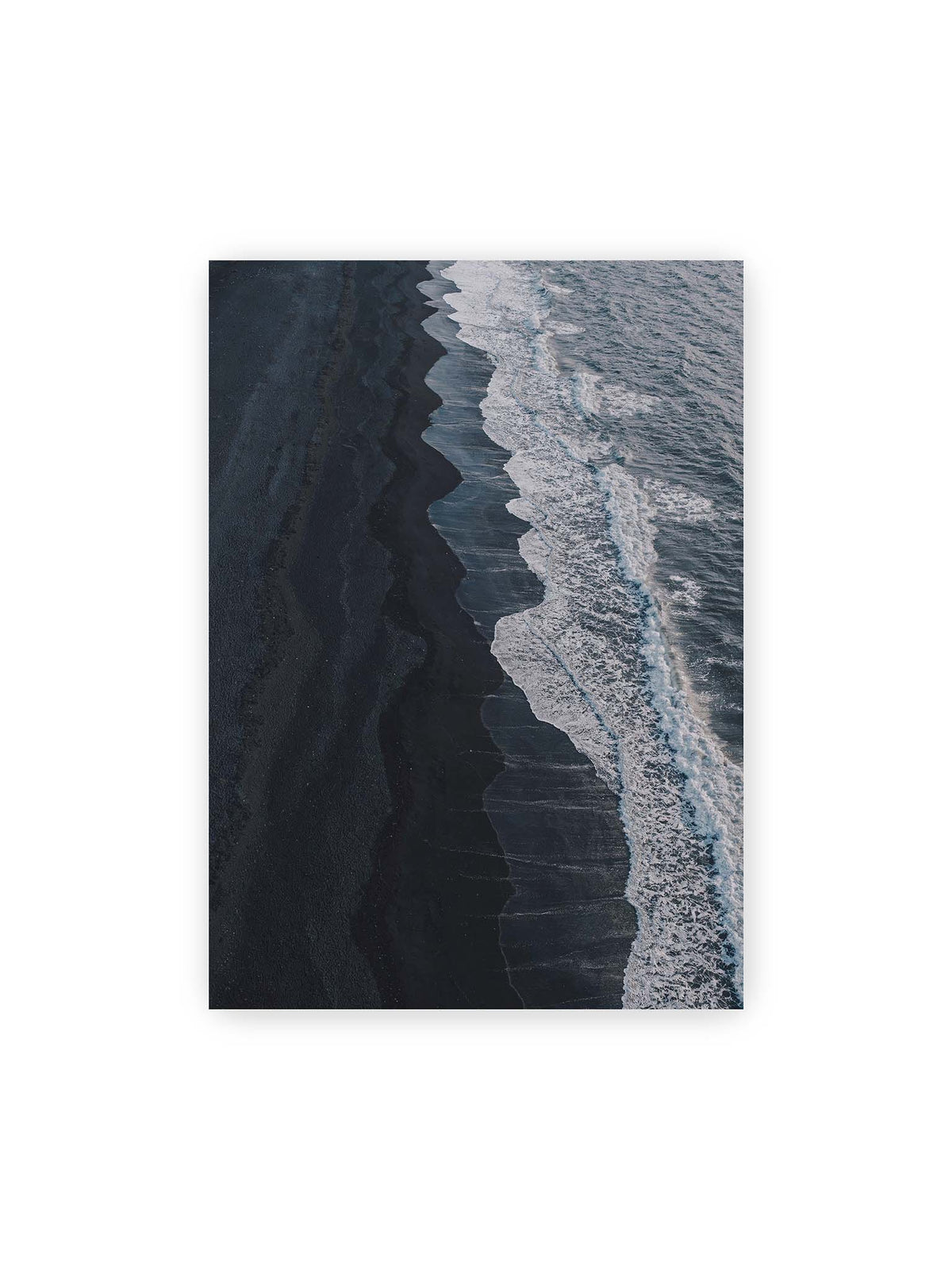 50x70 cm – Dunkler Strand aus erhöhter Perspektive mit weißer Brandung und blau-grauem Meer entlang einer geschwungenen Küstenlinie.