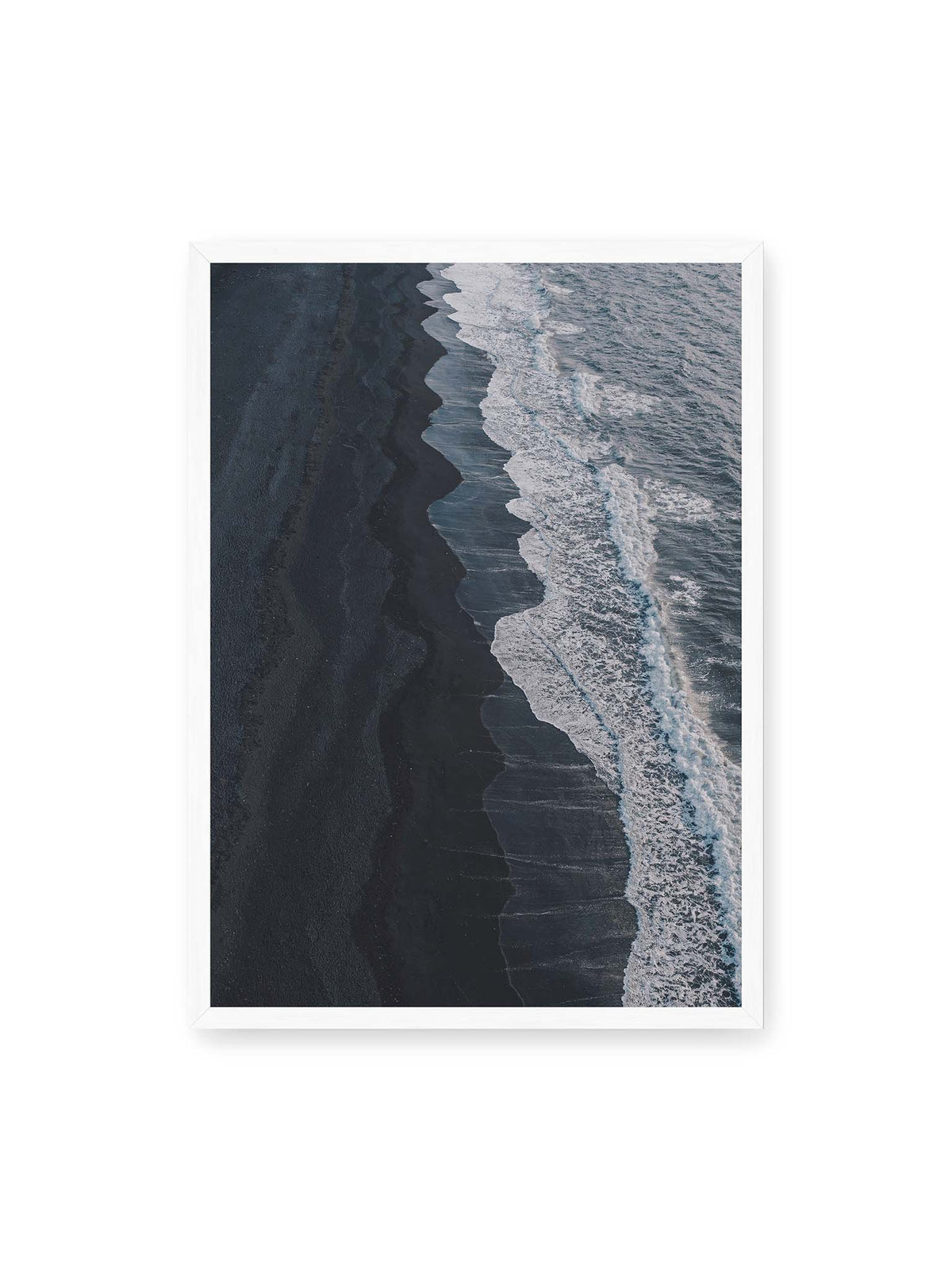 50x70 cm, weißer Rahmen – Dunkler Strand aus erhöhter Perspektive mit weißer Brandung und blau-grauem Meer entlang einer geschwungenen Küstenlinie.