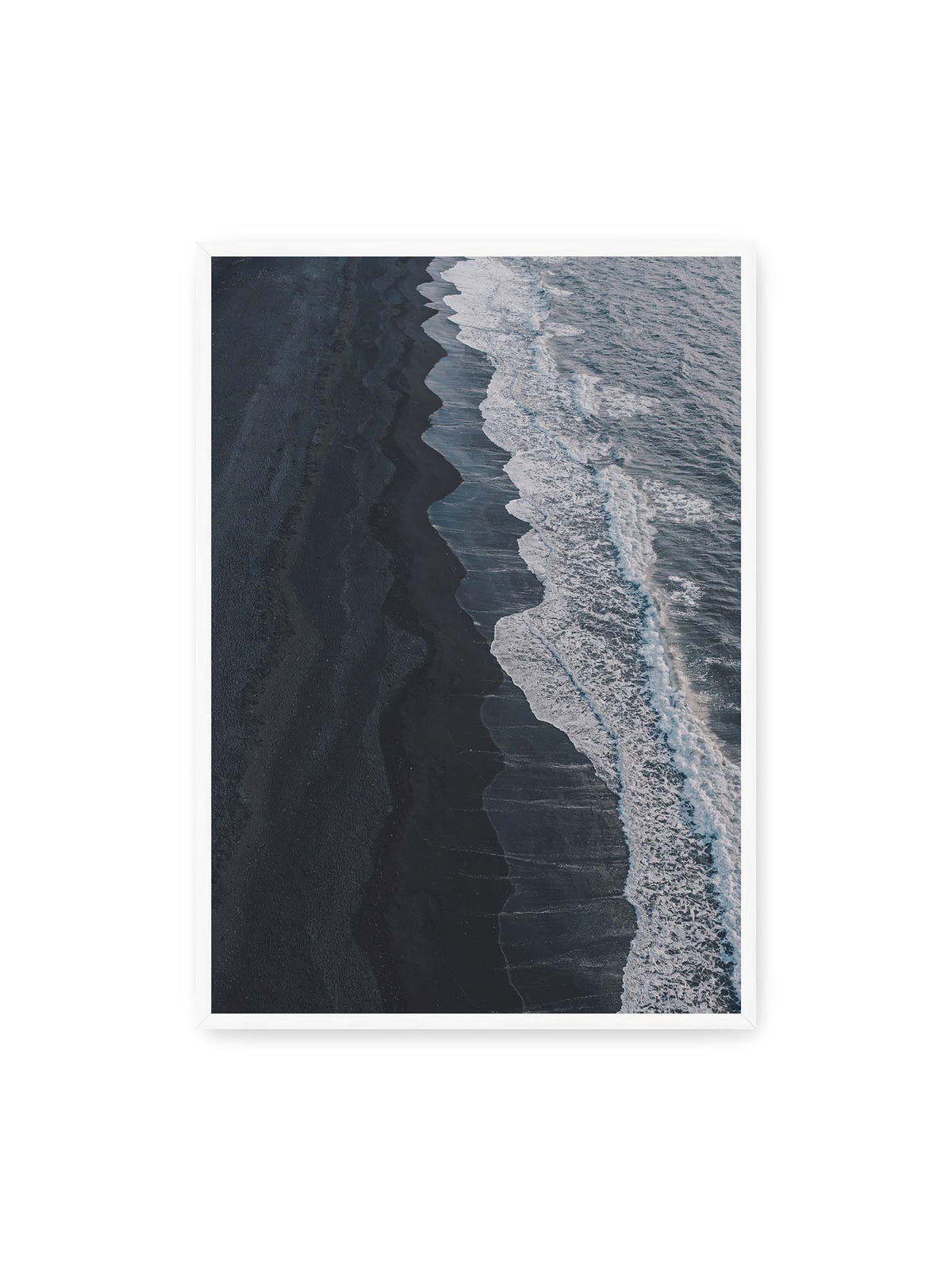 70x100 cm, weißer Rahmen – Dunkler Strand aus erhöhter Perspektive mit weißer Brandung und blau-grauem Meer entlang einer geschwungenen Küstenlinie.