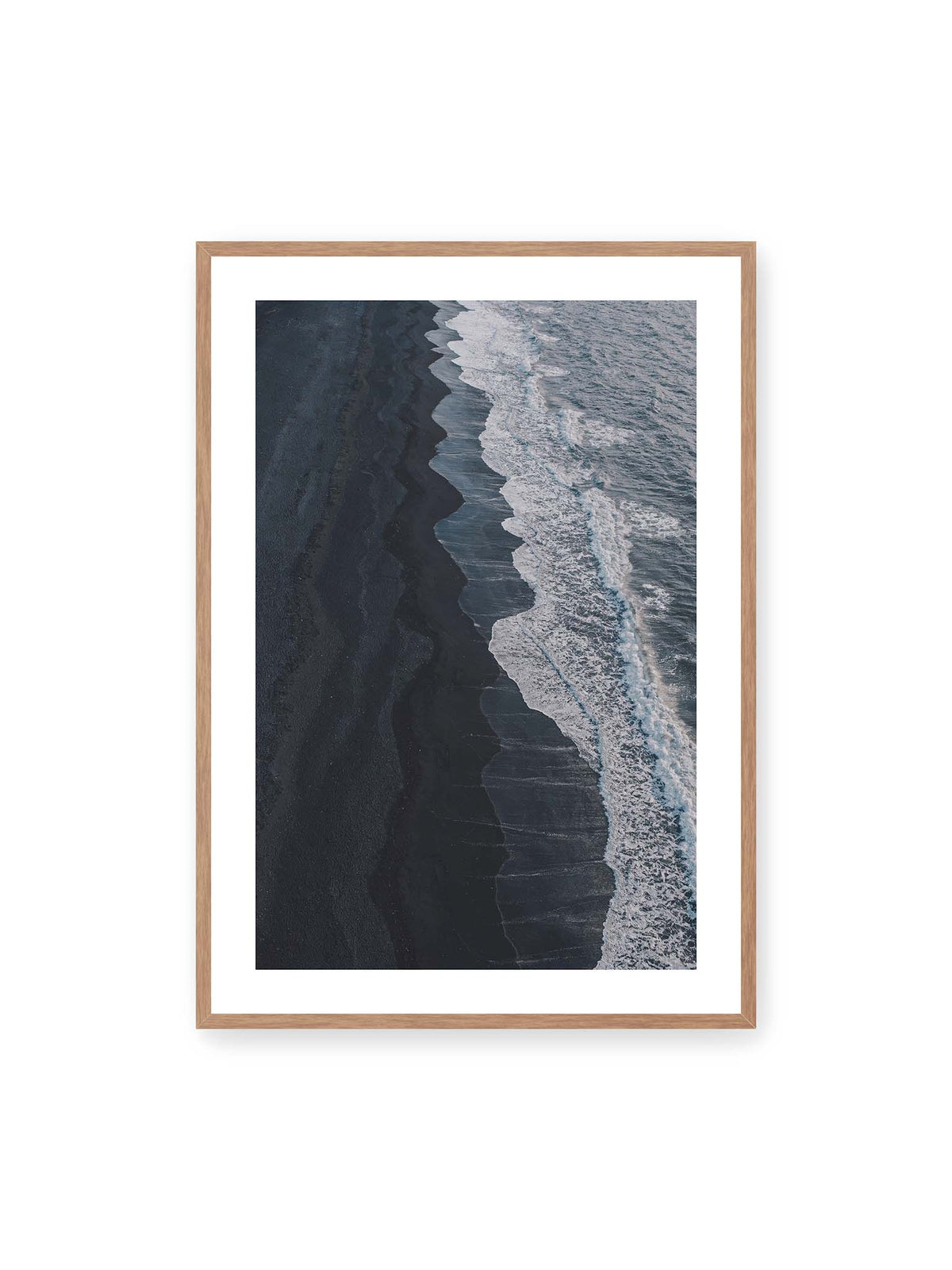 70x100 cm, weißer Galerie-Rand, Eichenrahmen – Dunkler Strand aus erhöhter Perspektive mit weißer Brandung und blau-grauem Meer entlang einer geschwungenen Küstenlinie.