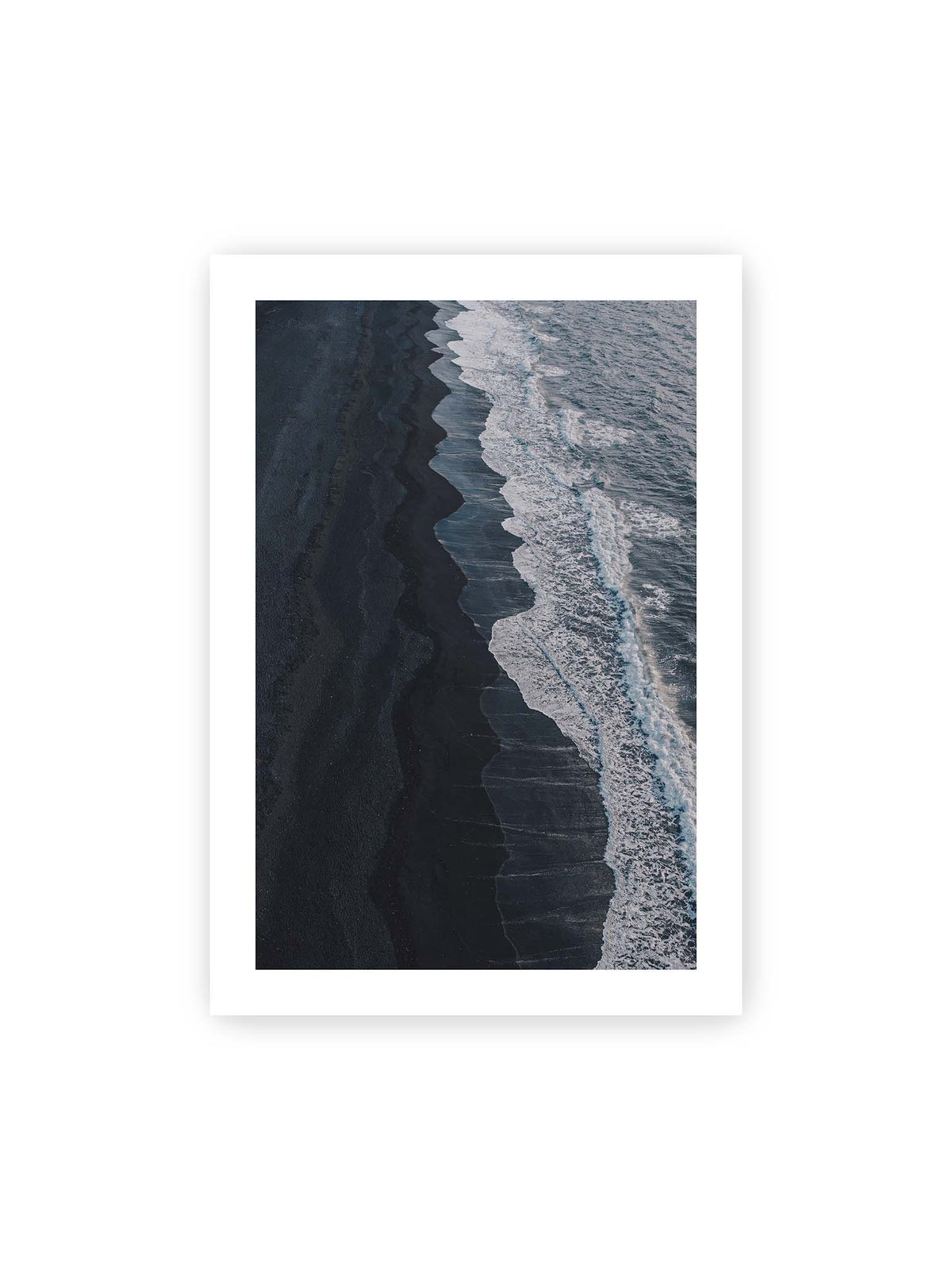70x100 cm, weißer Galerie-Rand – Dunkler Strand aus erhöhter Perspektive mit weißer Brandung und blau-grauem Meer entlang einer geschwungenen Küstenlinie.