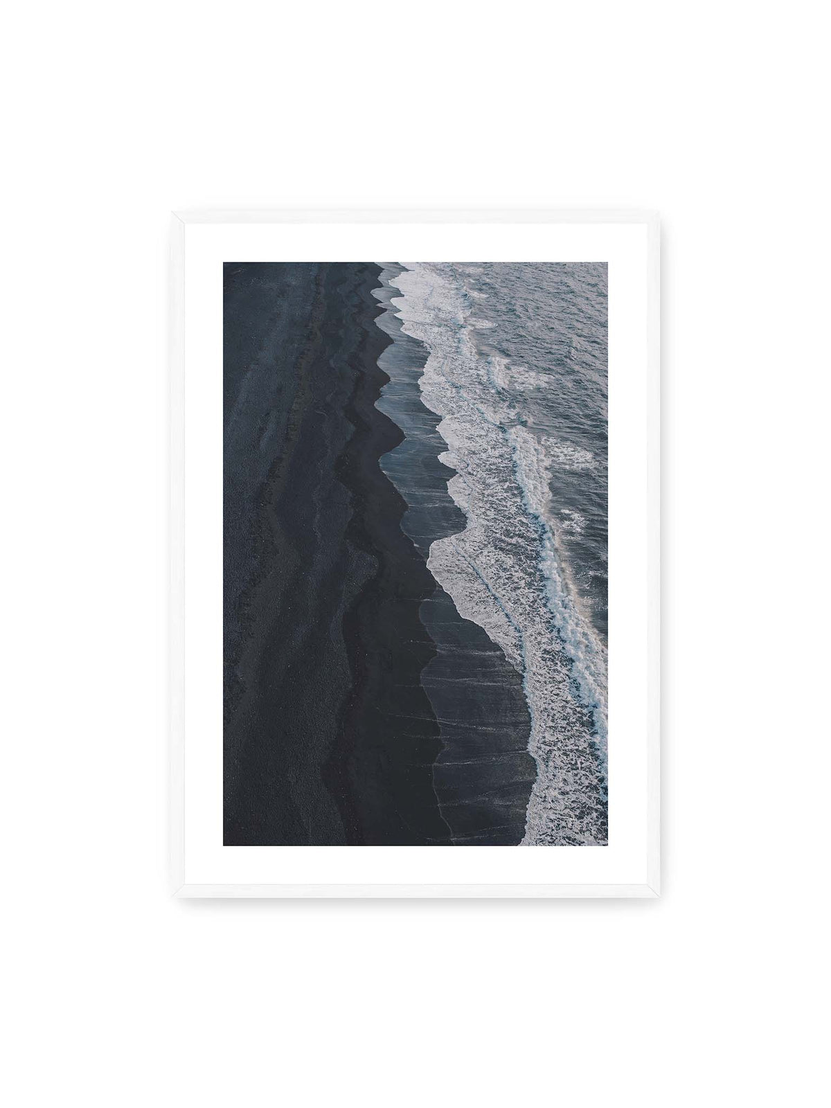 70x100 cm, weißer Galerie-Rand, weißer Rahmen – Dunkler Strand aus erhöhter Perspektive mit weißer Brandung und blau-grauem Meer entlang einer geschwungenen Küstenlinie.