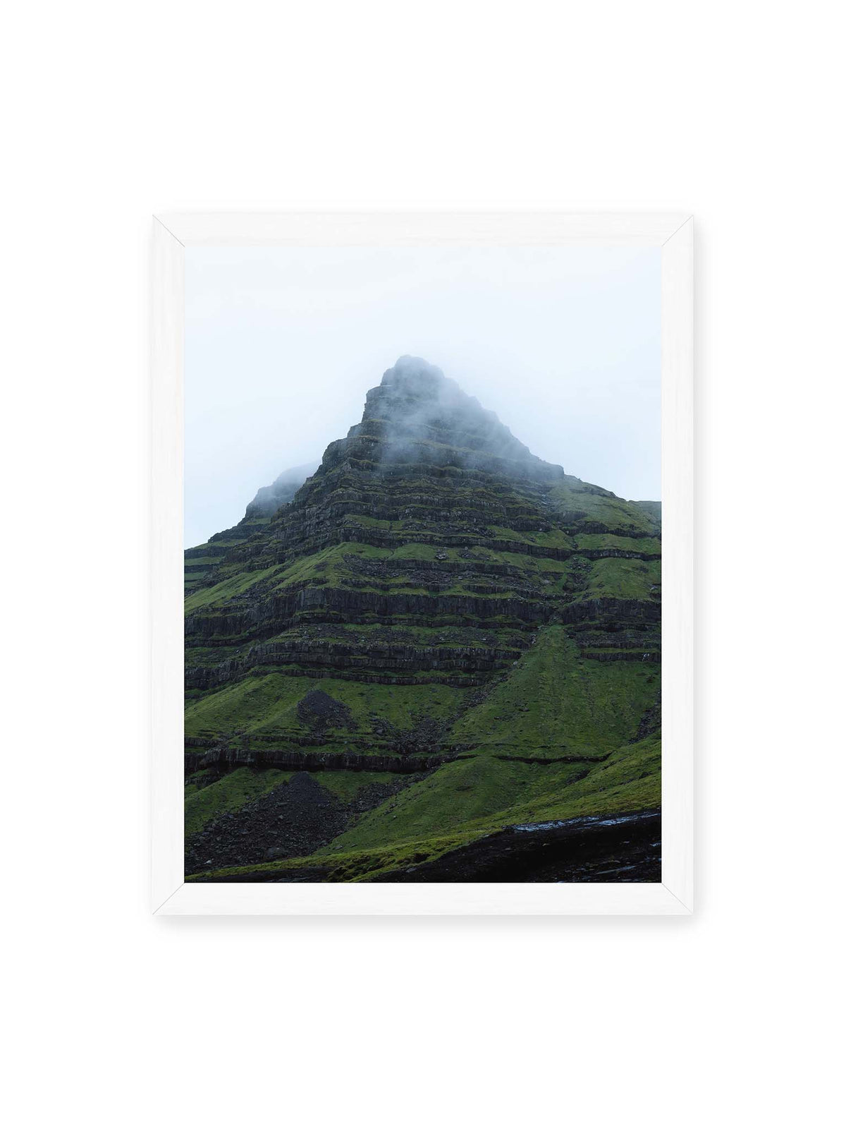 30x40 cm, weißer Rahmen – Steiler grüner Berg mit dunklen Felsbändern, dessen Gipfel in dichtem Nebel verschwindet.