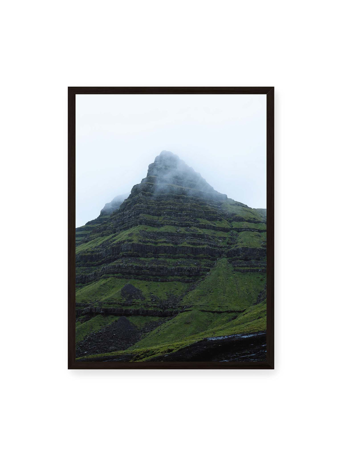 50x70 cm, schwarzer Rahmen – Steiler grüner Berg mit dunklen Felsbändern, dessen Gipfel in dichtem Nebel verschwindet.