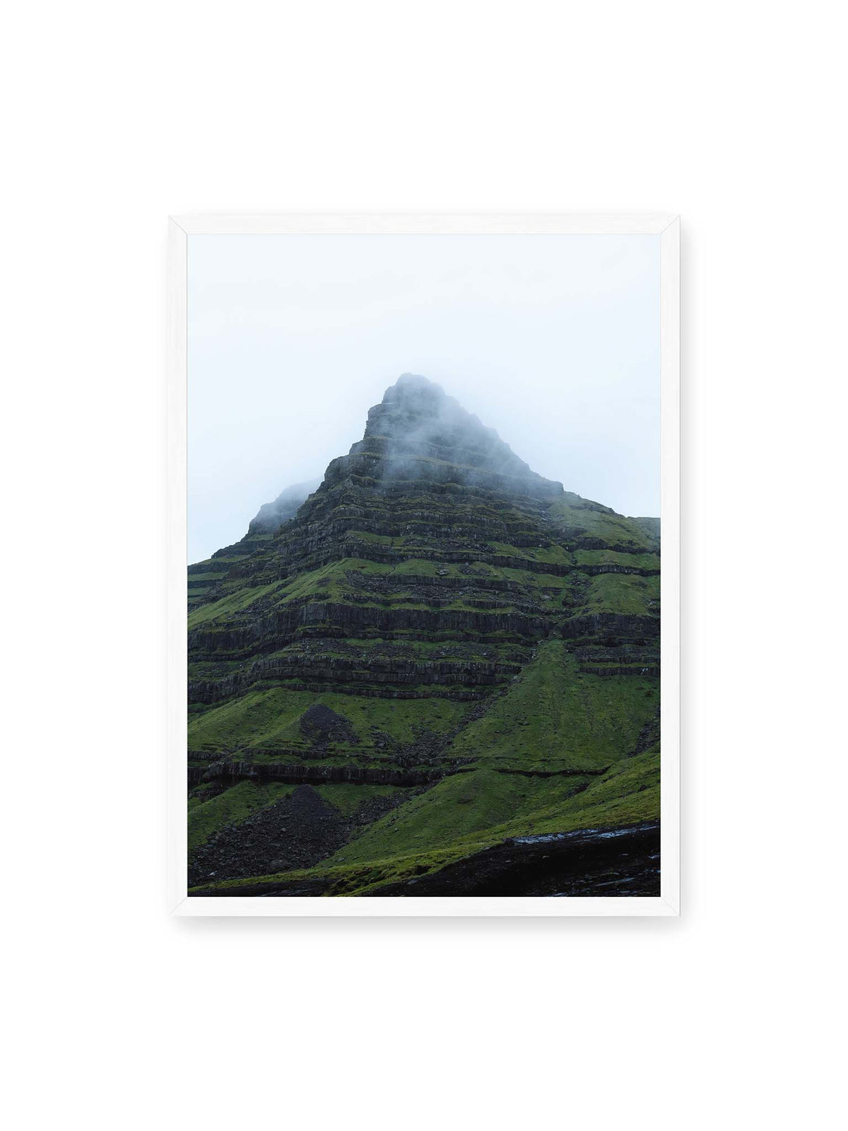 50x70 cm, weißer Rahmen – Steiler grüner Berg mit dunklen Felsbändern, dessen Gipfel in dichtem Nebel verschwindet.