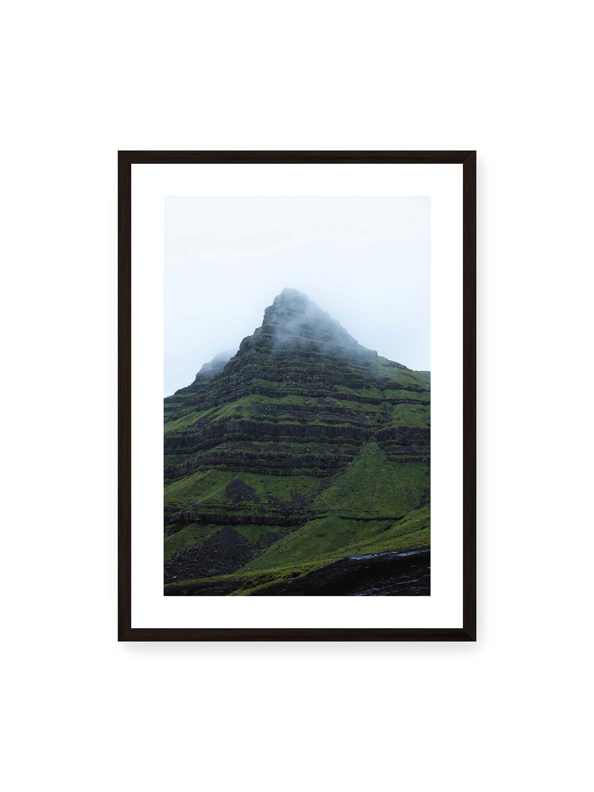 50x70 cm, weißer Galerie-Rand, schwarzer Rahmen – Steiler grüner Berg mit dunklen Felsbändern, dessen Gipfel in dichtem Nebel verschwindet.