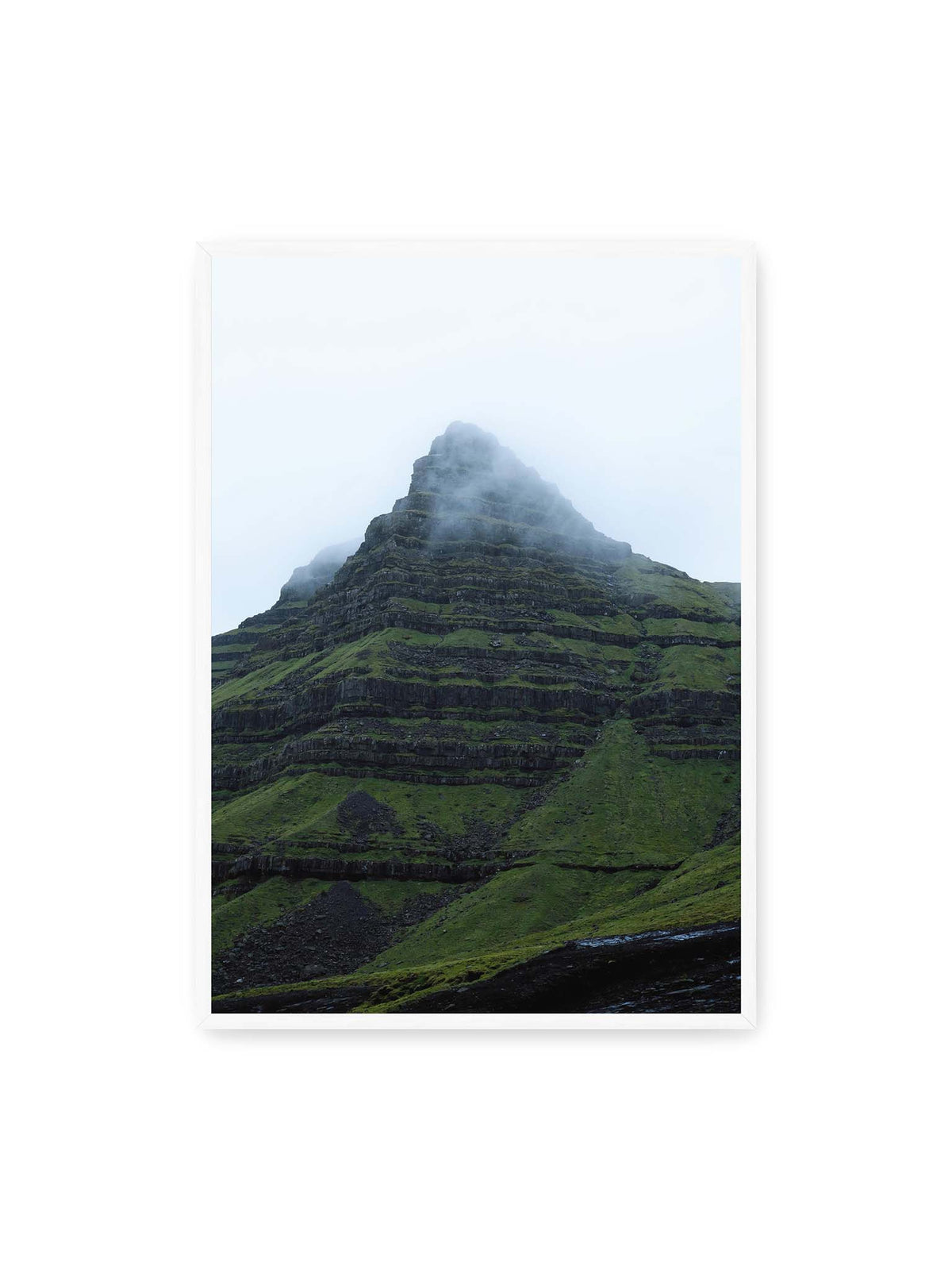 70x100 cm, weißer Rahmen – Steiler grüner Berg mit dunklen Felsbändern, dessen Gipfel in dichtem Nebel verschwindet.
