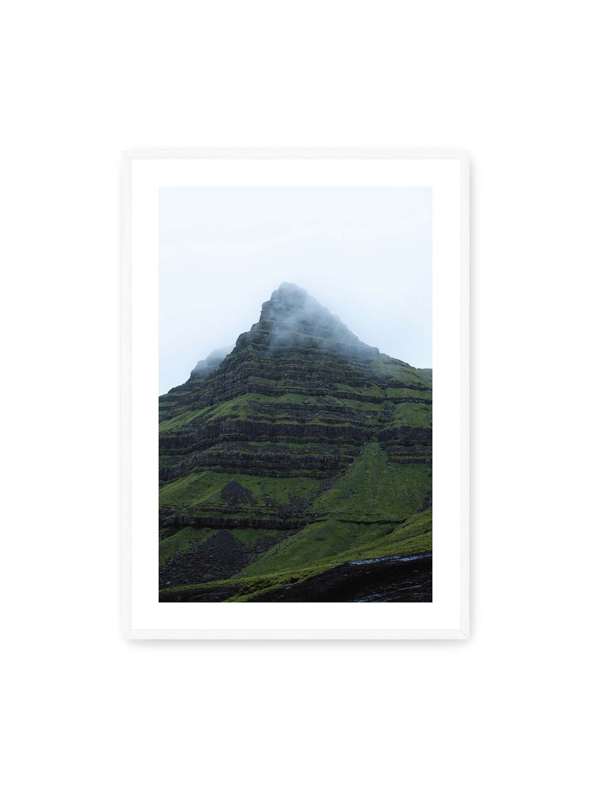 70x100 cm, weißer Galerie-Rand, weißer Rahmen – Steiler grüner Berg mit dunklen Felsbändern, dessen Gipfel in dichtem Nebel verschwindet.