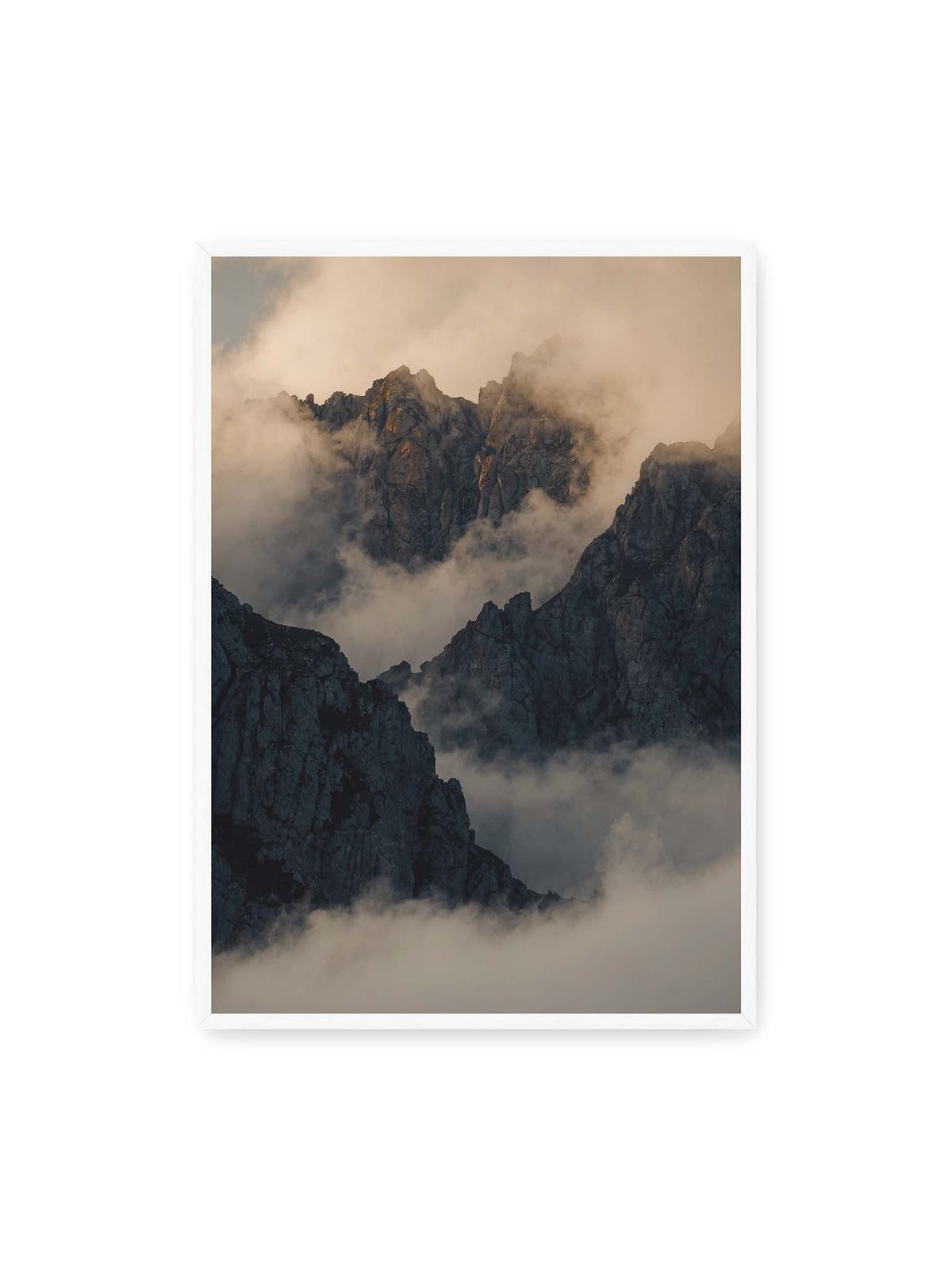 70x100 cm, weißer Rahmen – Zerklüftete dunkle Bergspitzen zwischen dichten Wolken mit warm beleuchteten Felsflächen.
