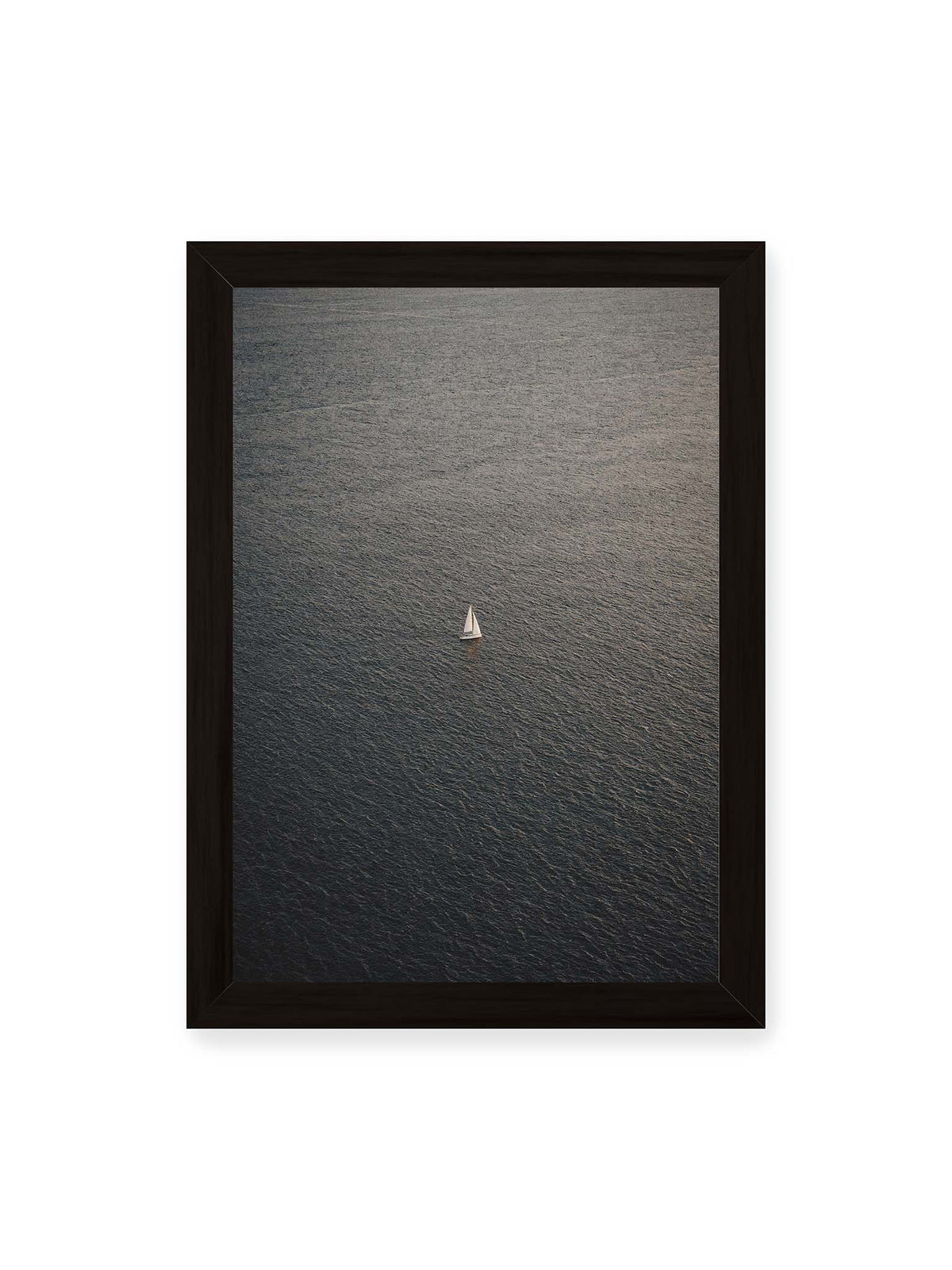 21x30 cm, schwarzer Rahmen – Einzelnes weißes Segelboot auf einer weitläufigen, dunkel strukturierten Wasserfläche aus erhöhter Perspektive.