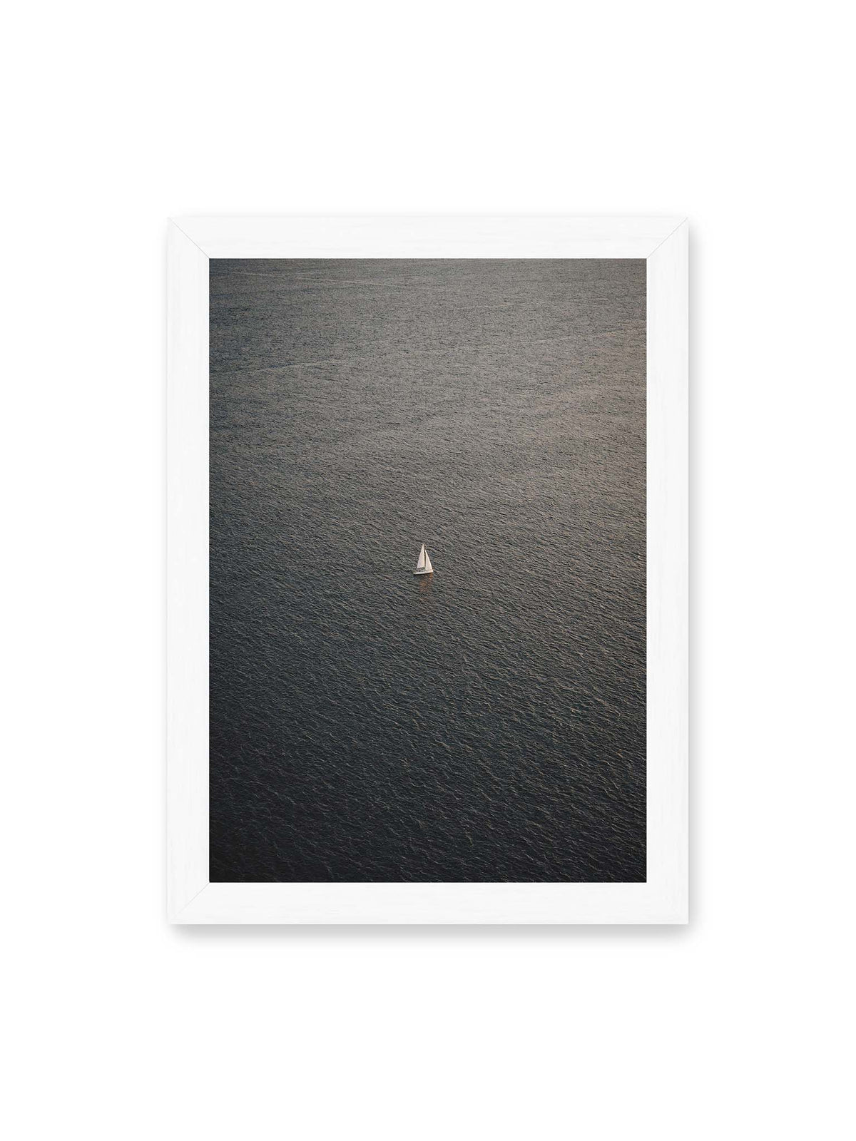 21x30 cm, weißer Rahmen – Einzelnes weißes Segelboot auf einer weitläufigen, dunkel strukturierten Wasserfläche aus erhöhter Perspektive.