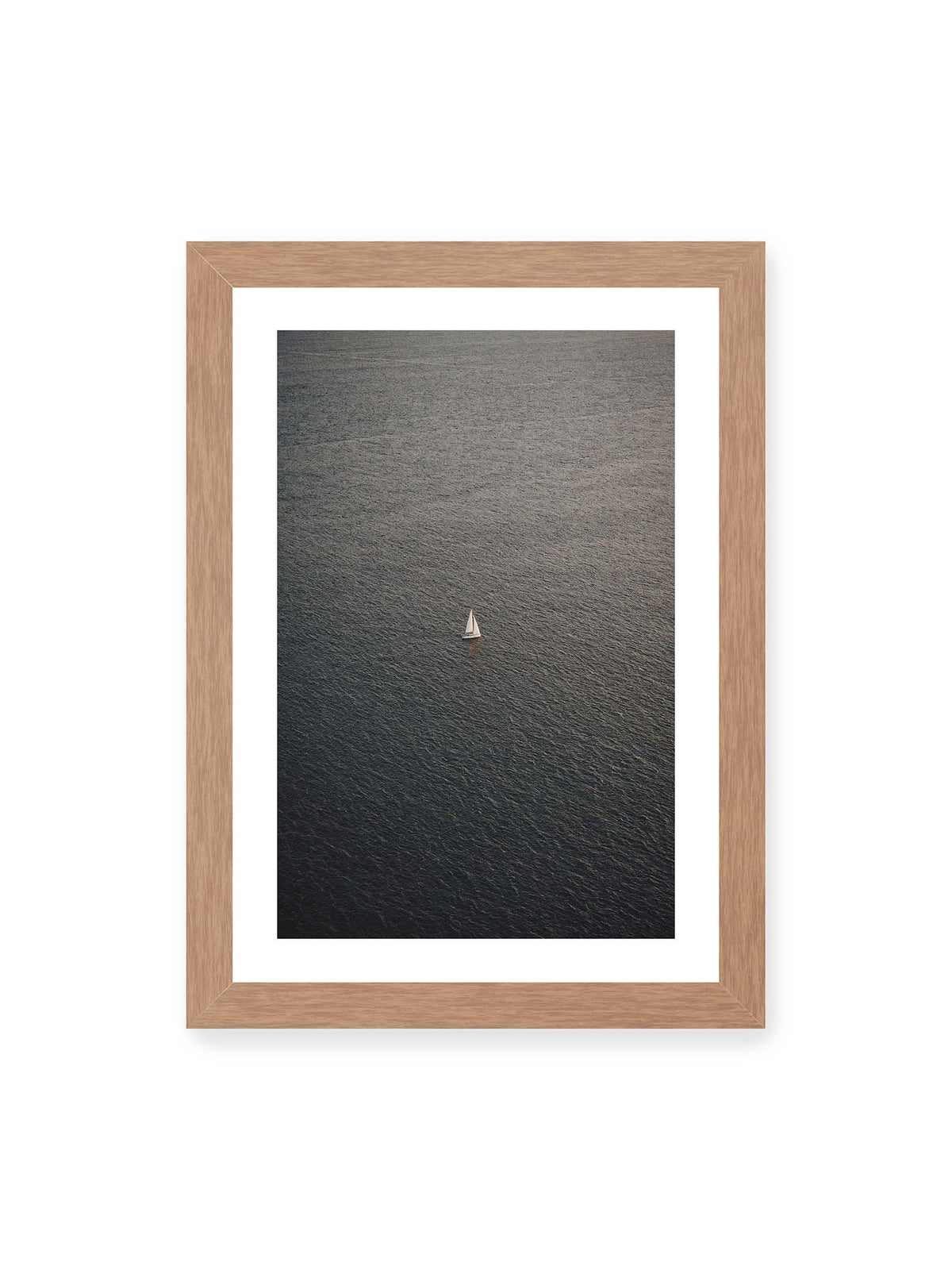 21x30 cm, weißer Galerie-Rand, Eichenrahmen – Einzelnes weißes Segelboot auf einer weitläufigen, dunkel strukturierten Wasserfläche aus erhöhter Perspektive.