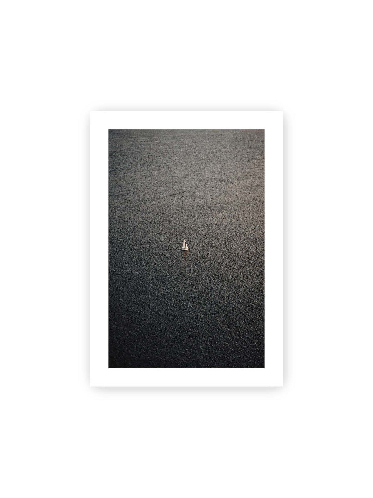 21x30 cm, weißer Galerie-Rand – Einzelnes weißes Segelboot auf einer weitläufigen, dunkel strukturierten Wasserfläche aus erhöhter Perspektive.