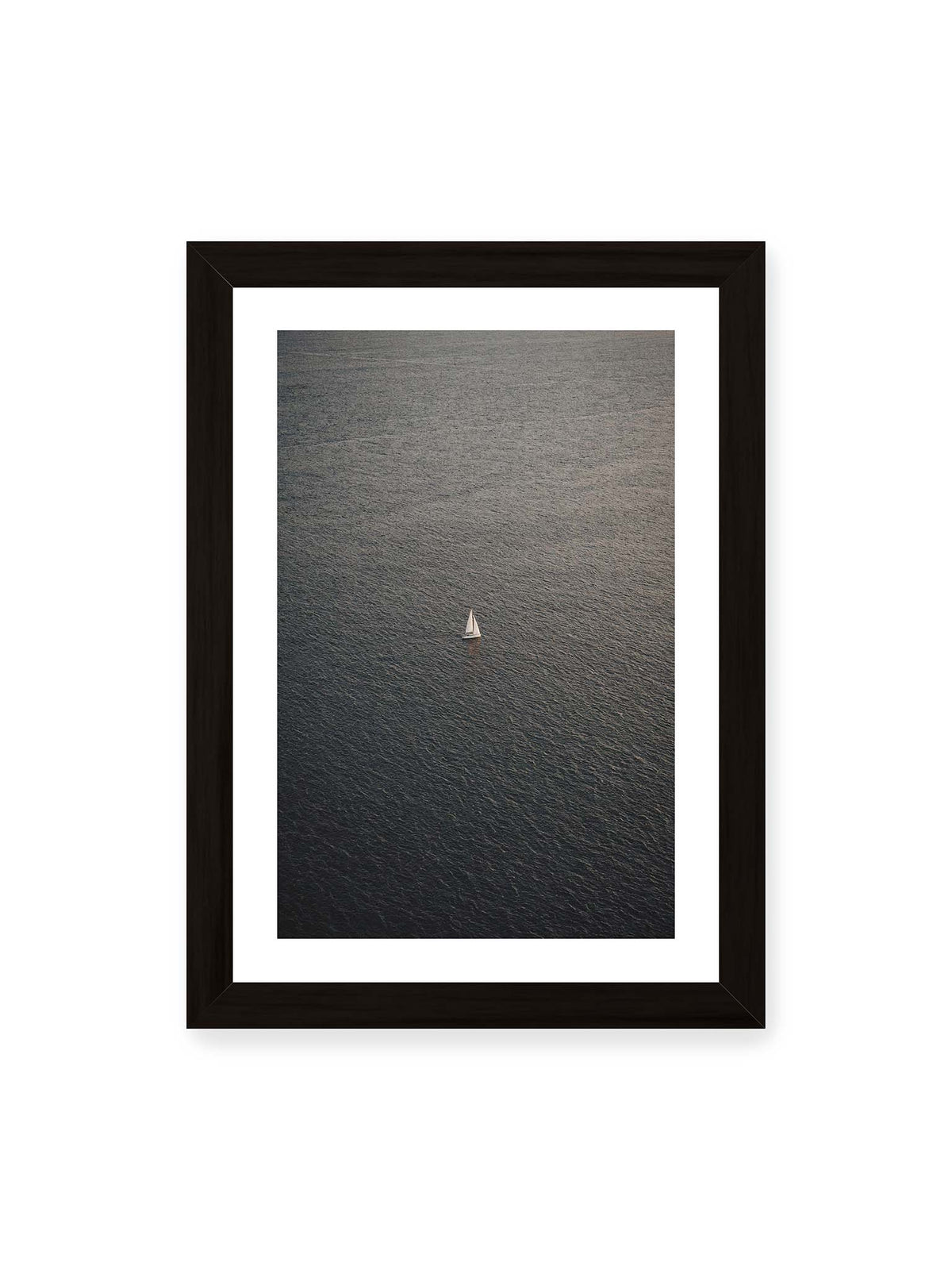 21x30 cm, weißer Galerie-Rand, schwarzer Rahmen – Einzelnes weißes Segelboot auf einer weitläufigen, dunkel strukturierten Wasserfläche aus erhöhter Perspektive.