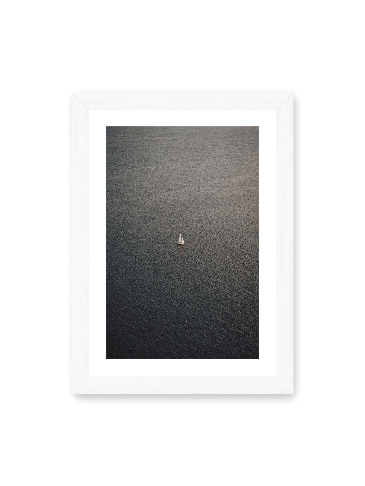 21x30 cm, weißer Galerie-Rand, weißer Rahmen – Einzelnes weißes Segelboot auf einer weitläufigen, dunkel strukturierten Wasserfläche aus erhöhter Perspektive.