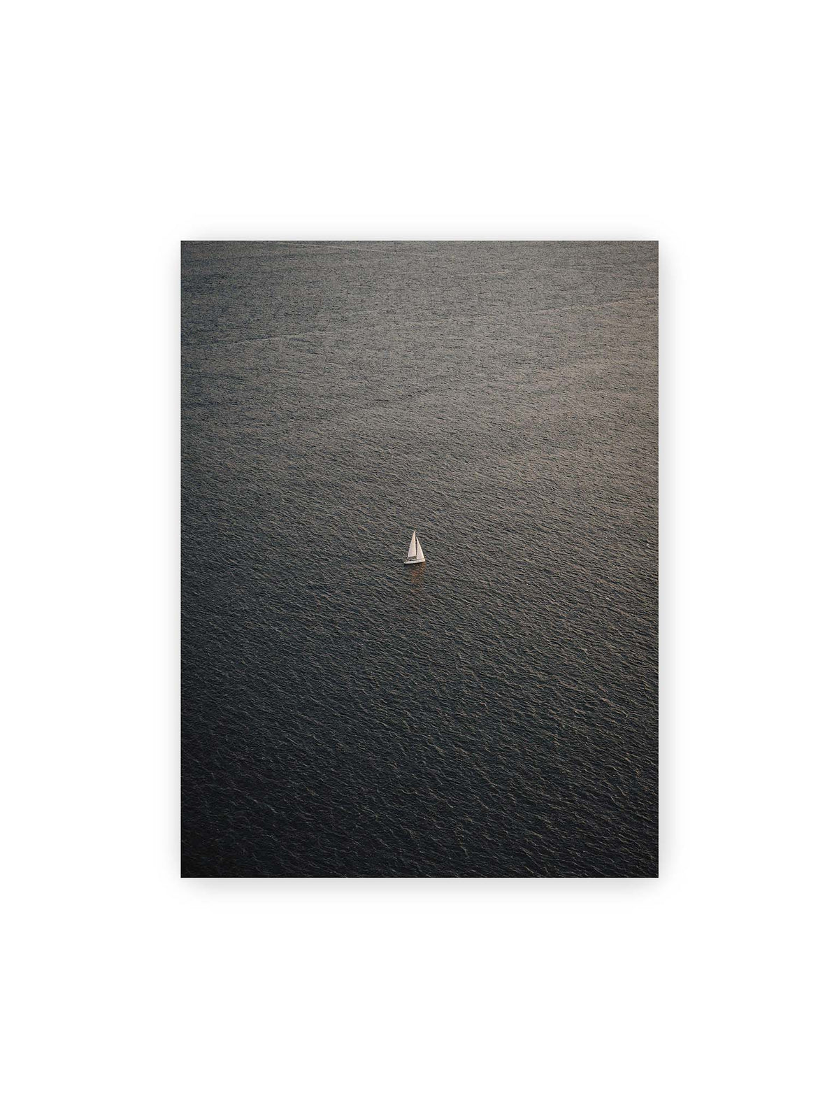 30x40 cm – Einzelnes weißes Segelboot auf einer weitläufigen, dunkel strukturierten Wasserfläche aus erhöhter Perspektive.