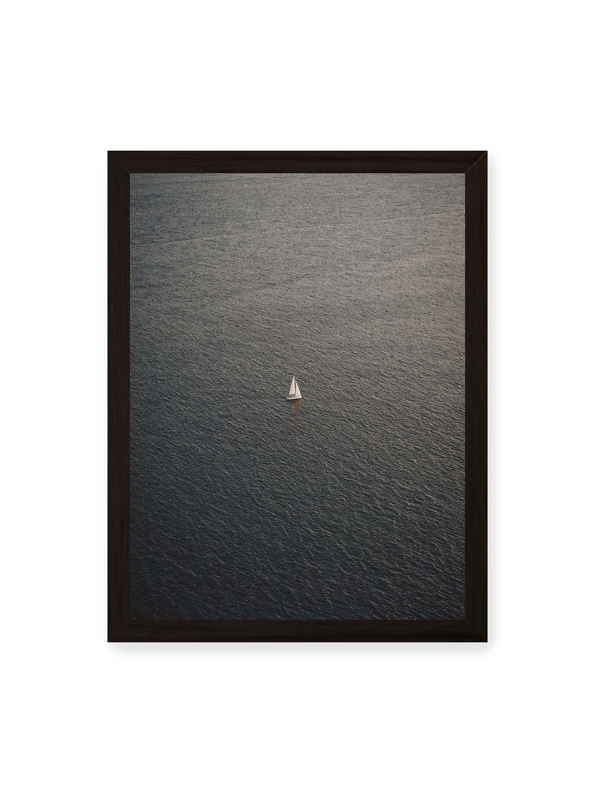 30x40 cm, schwarzer Rahmen – Einzelnes weißes Segelboot auf einer weitläufigen, dunkel strukturierten Wasserfläche aus erhöhter Perspektive.