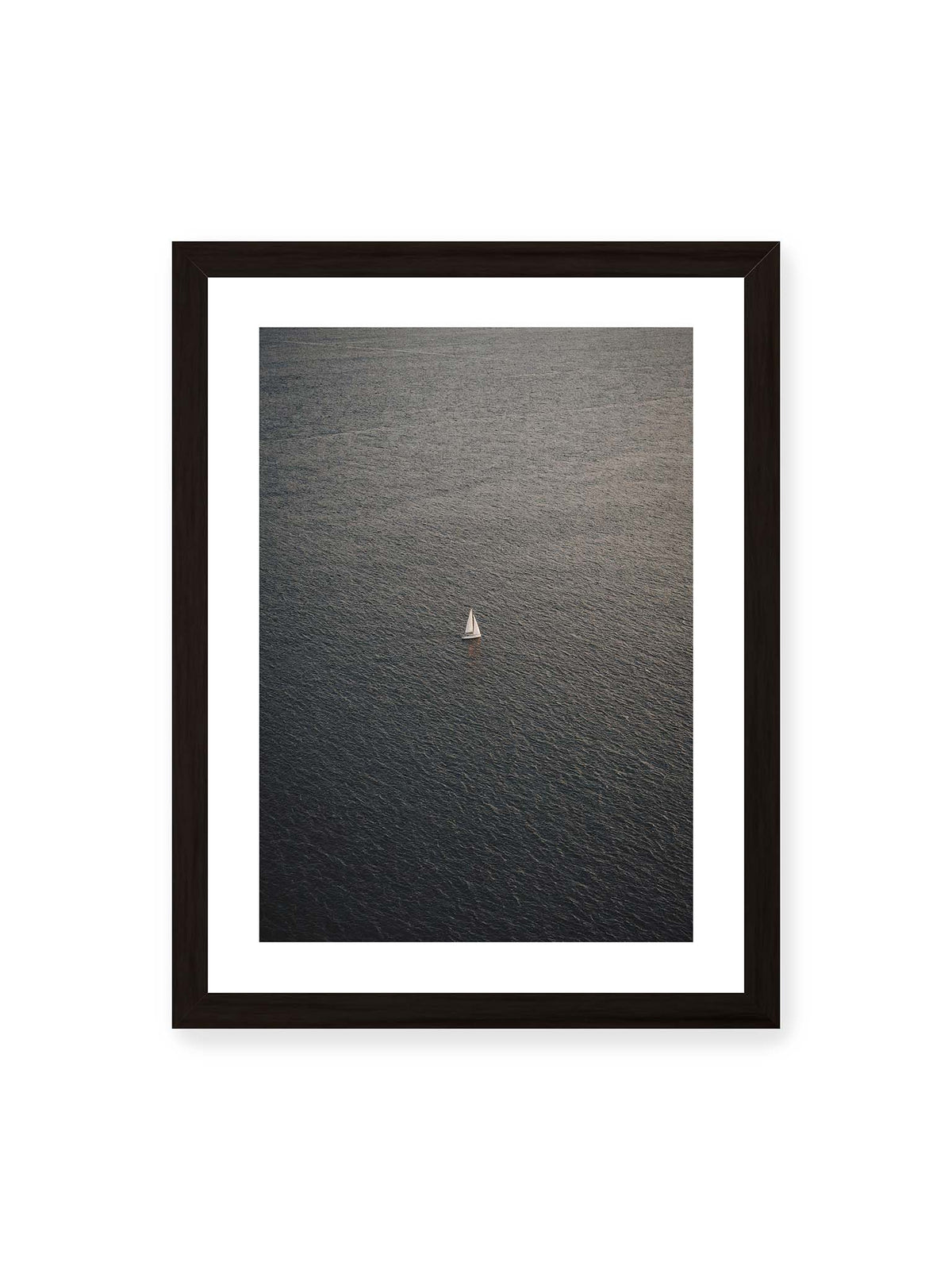 30x40 cm, weißer Galerie-Rand, schwarzer Rahmen – Einzelnes weißes Segelboot auf einer weitläufigen, dunkel strukturierten Wasserfläche aus erhöhter Perspektive.
