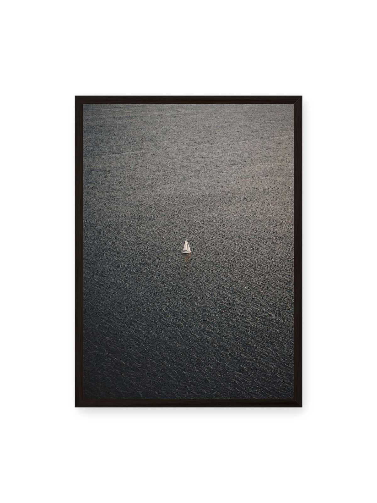 50x70 cm, schwarzer Rahmen – Einzelnes weißes Segelboot auf einer weitläufigen, dunkel strukturierten Wasserfläche aus erhöhter Perspektive.