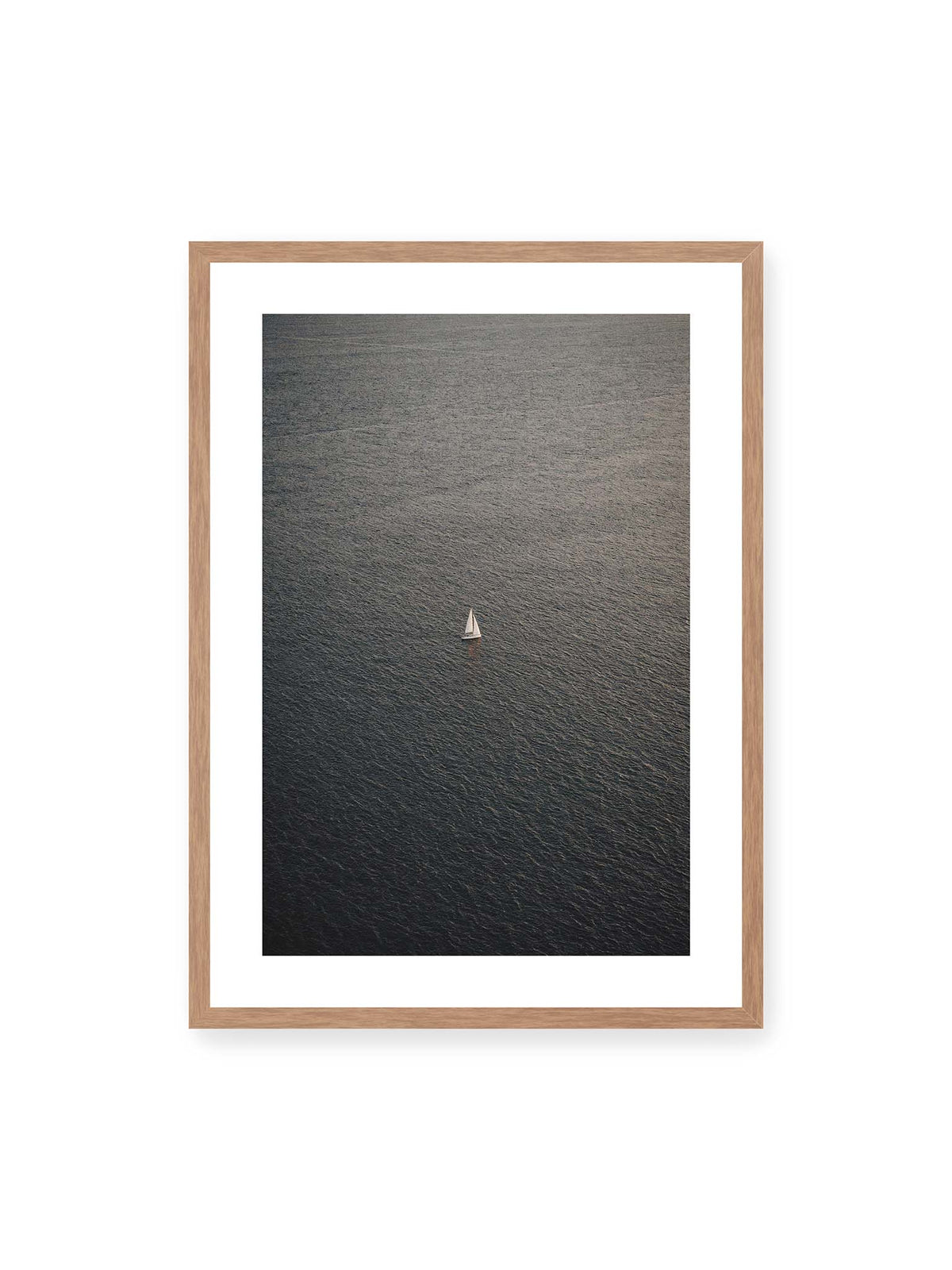 50x70 cm, weißer Galerie-Rand, Eichenrahmen – Einzelnes weißes Segelboot auf einer weitläufigen, dunkel strukturierten Wasserfläche aus erhöhter Perspektive.