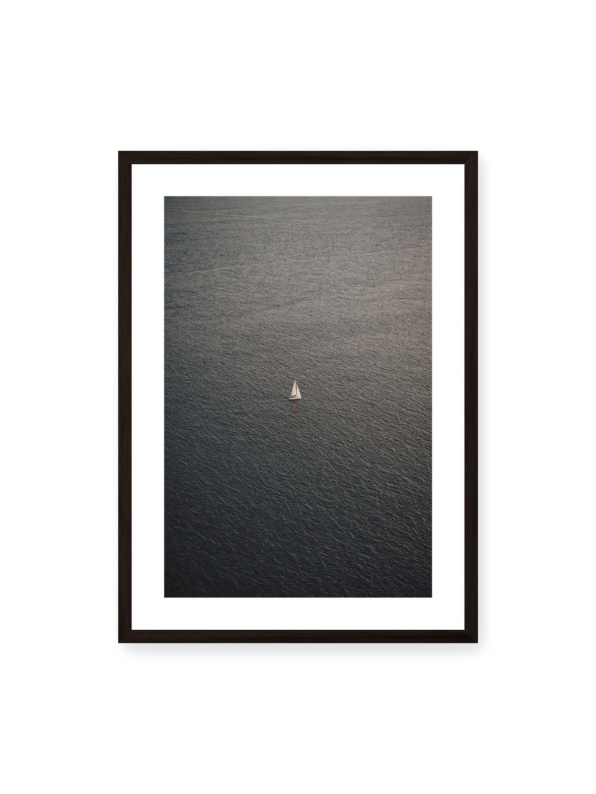 50x70 cm, weißer Galerie-Rand, schwarzer Rahmen – Einzelnes weißes Segelboot auf einer weitläufigen, dunkel strukturierten Wasserfläche aus erhöhter Perspektive.