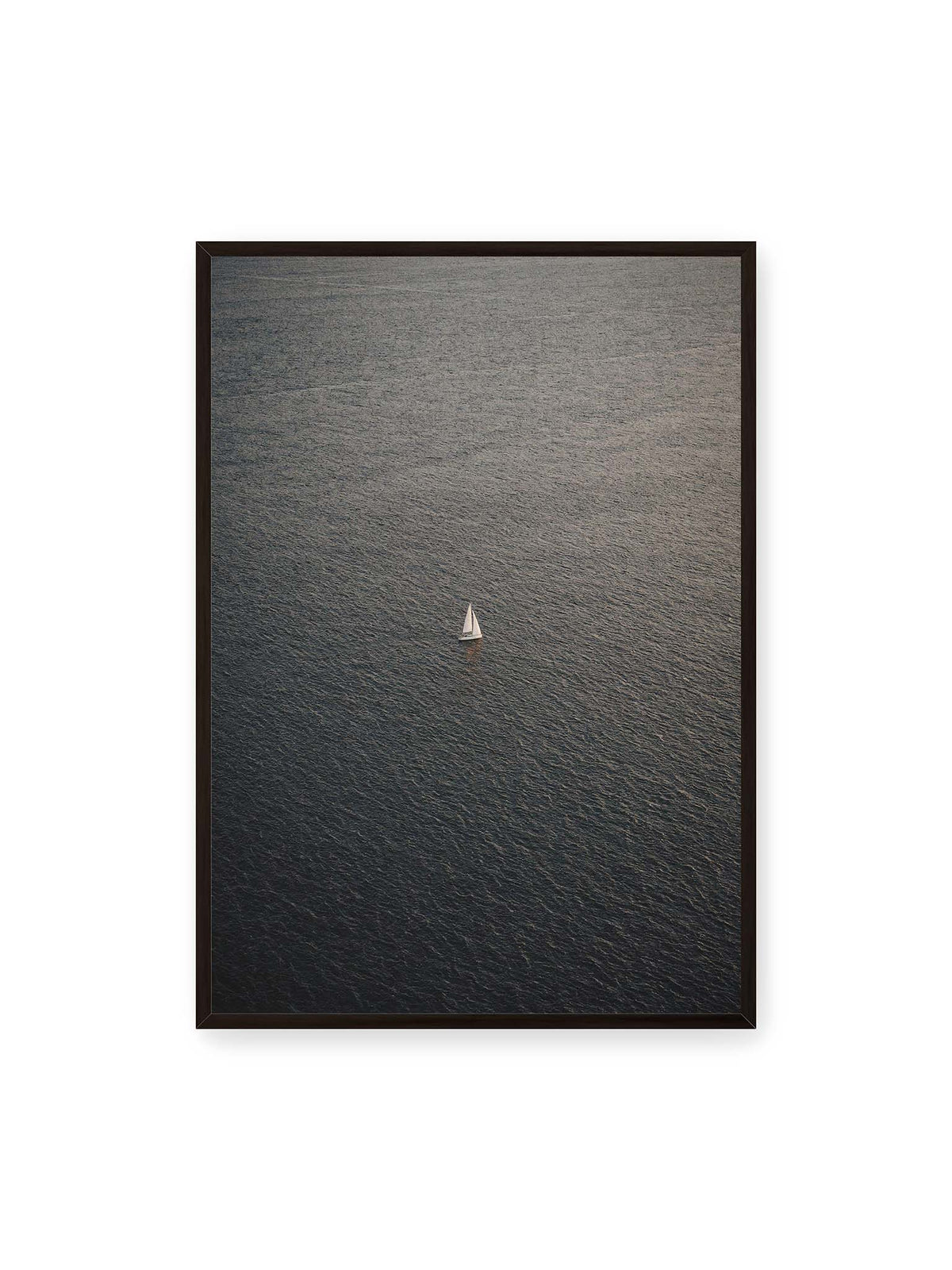 70x100 cm, schwarzer Rahmen – Einzelnes weißes Segelboot auf einer weitläufigen, dunkel strukturierten Wasserfläche aus erhöhter Perspektive.