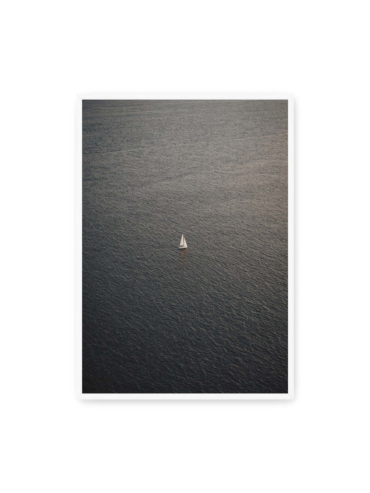 70x100 cm, weißer Rahmen – Einzelnes weißes Segelboot auf einer weitläufigen, dunkel strukturierten Wasserfläche aus erhöhter Perspektive.