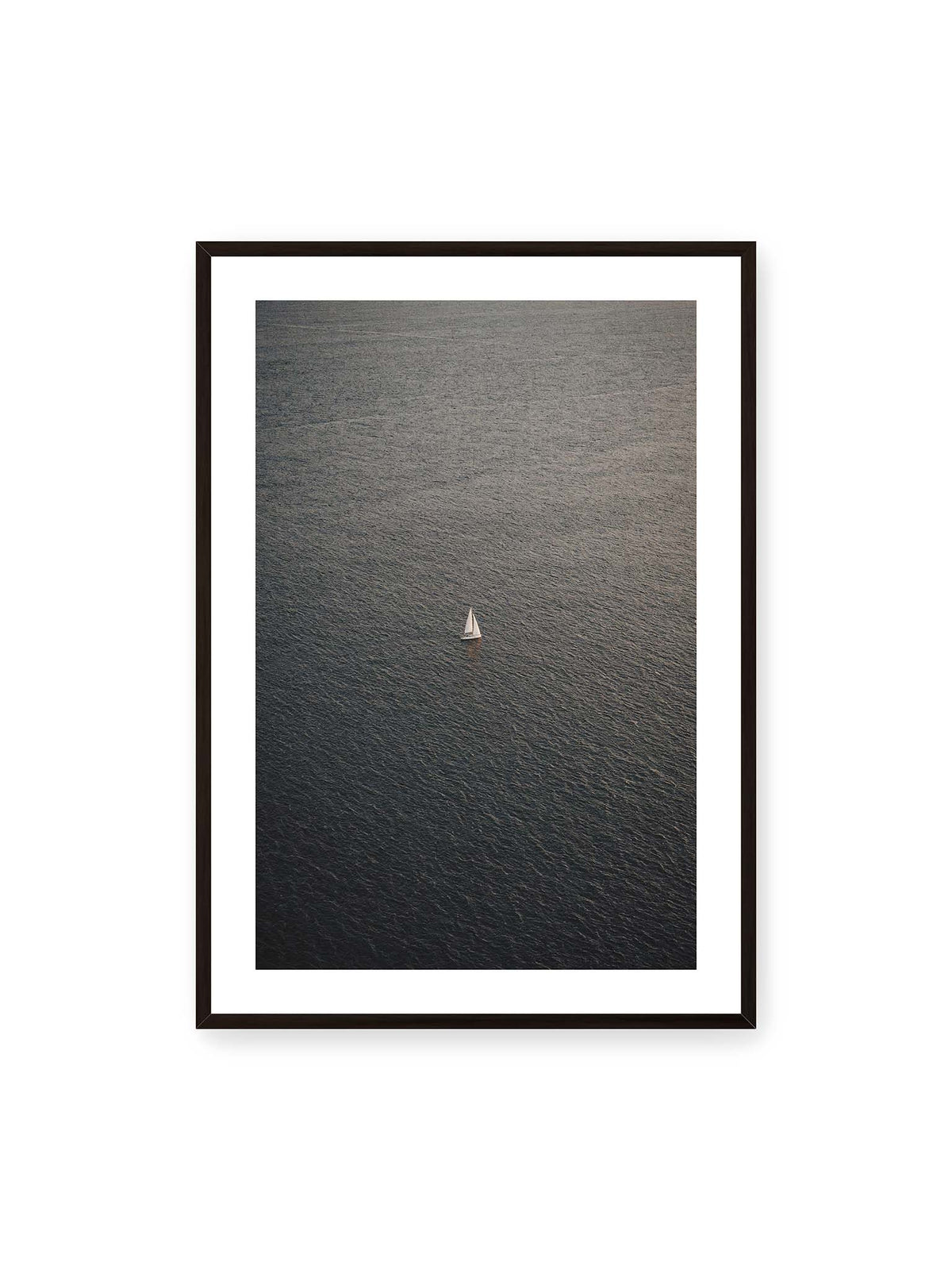 70x100 cm, weißer Galerie-Rand, schwarzer Rahmen – Einzelnes weißes Segelboot auf einer weitläufigen, dunkel strukturierten Wasserfläche aus erhöhter Perspektive.