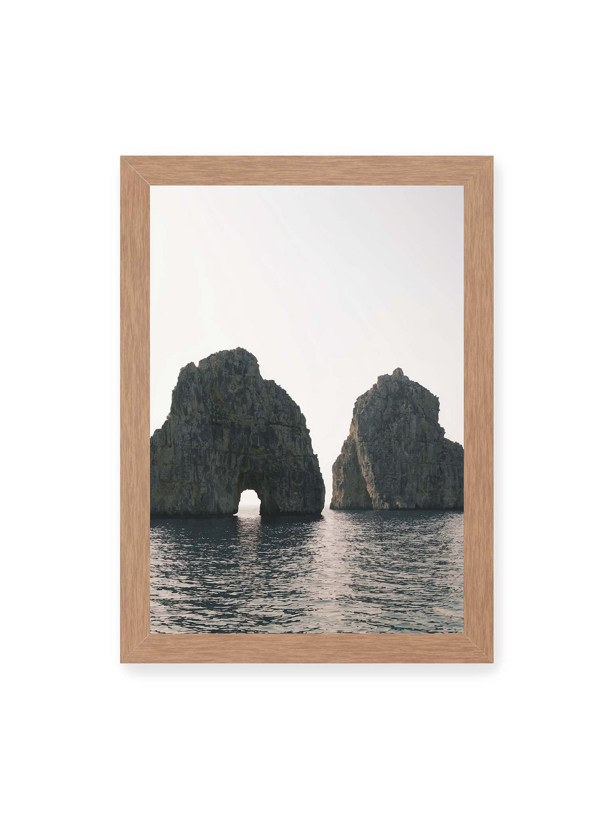 21x30 cm, Eichenrahmen – Zwei massive Felsformationen im Meer, eine mit natürlichem Felsbogen, vor hellem Himmel.