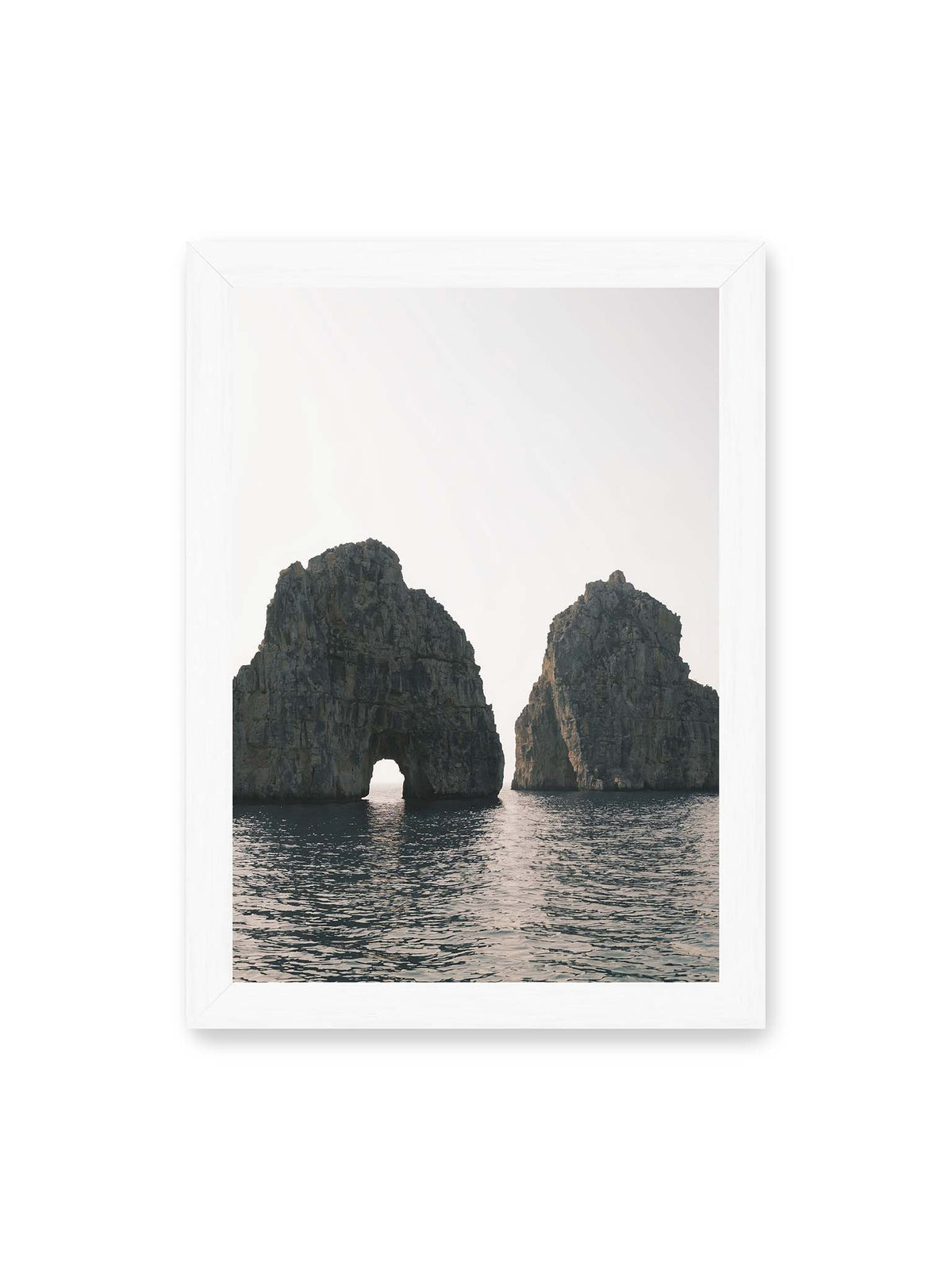 21x30 cm, weißer Rahmen – Zwei massive Felsformationen im Meer, eine mit natürlichem Felsbogen, vor hellem Himmel.