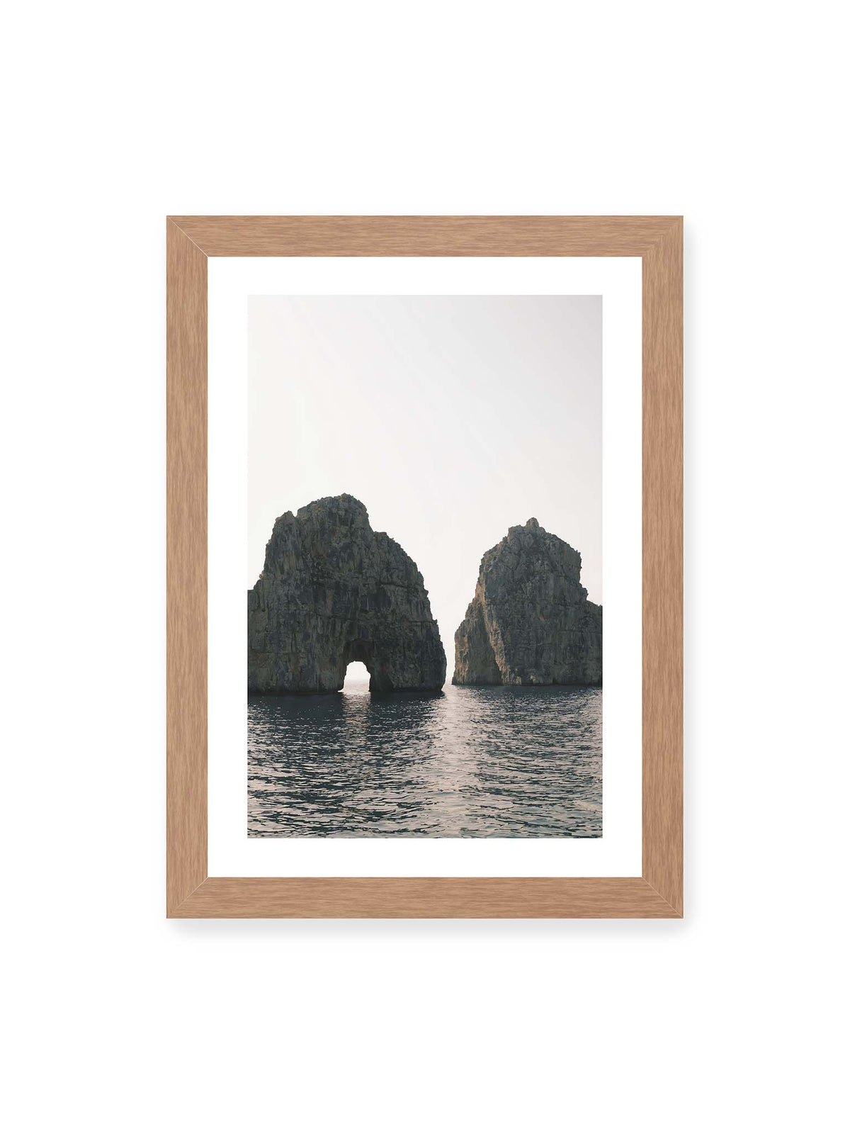 21x30 cm, weißer Galerie-Rand, Eichenrahmen – Zwei massive Felsformationen im Meer, eine mit natürlichem Felsbogen, vor hellem Himmel.