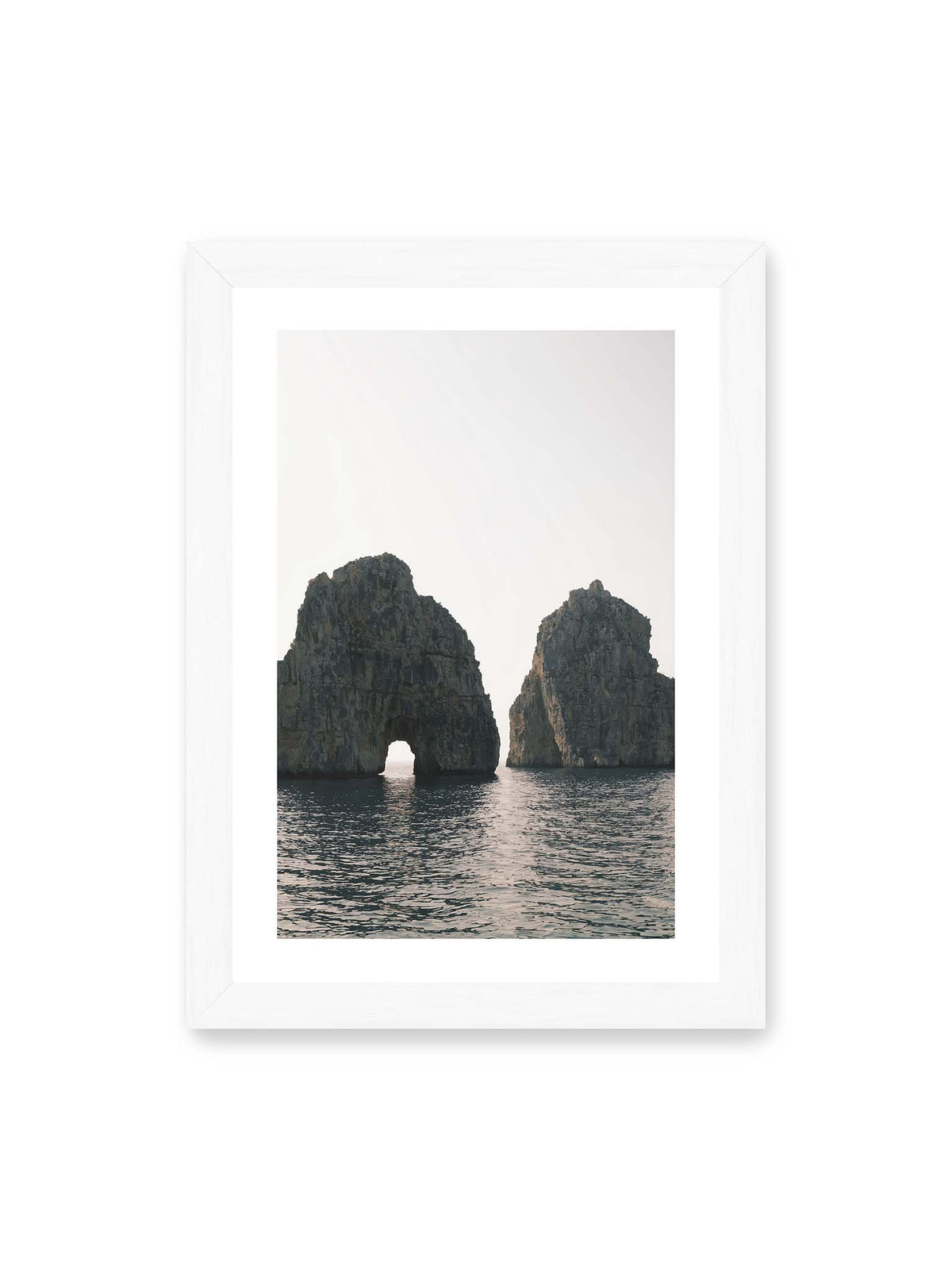 21x30 cm, weißer Galerie-Rand, weißer Rahmen – Zwei massive Felsformationen im Meer, eine mit natürlichem Felsbogen, vor hellem Himmel.