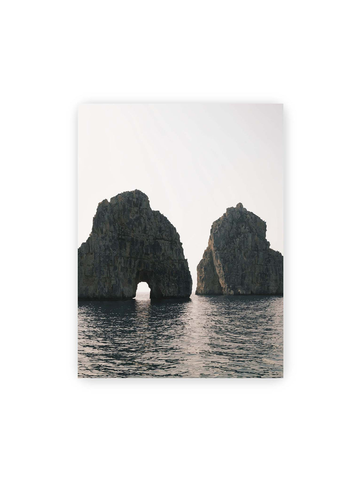 30x40 cm – Zwei massive Felsformationen im Meer, eine mit natürlichem Felsbogen, vor hellem Himmel.