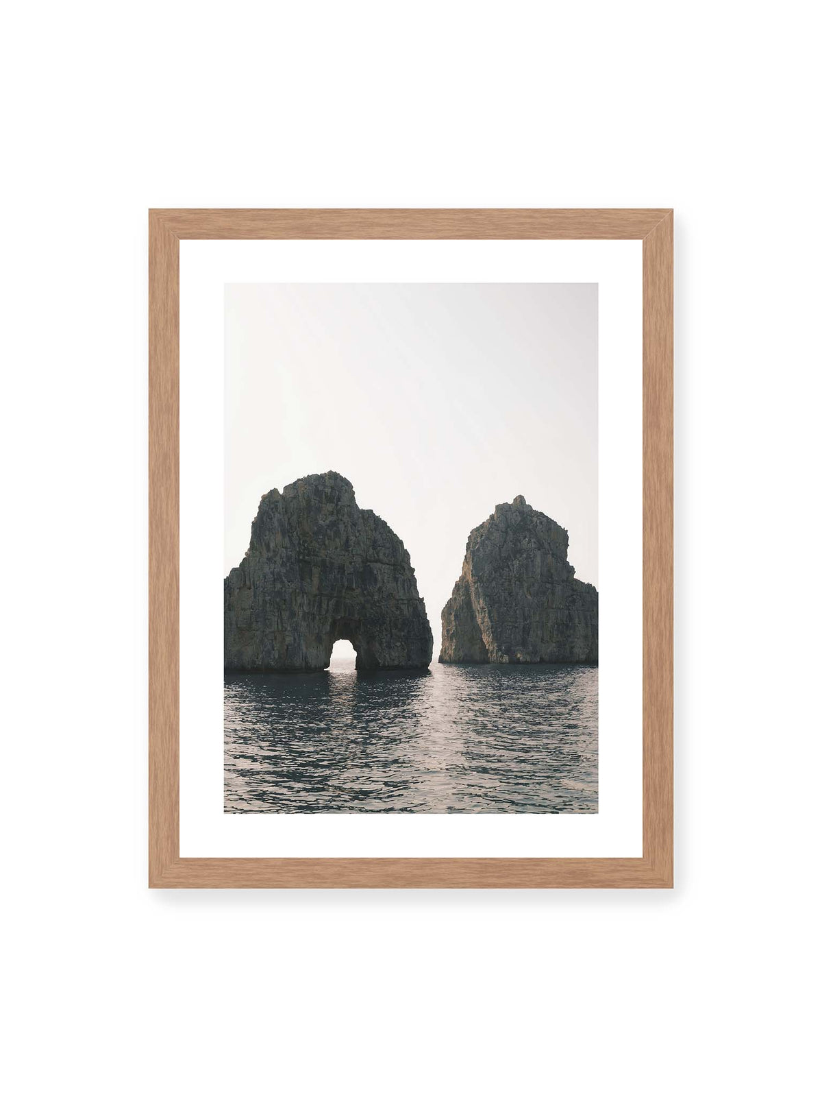 30x40 cm, weißer Galerie-Rand, Eichenrahmen – Zwei massive Felsformationen im Meer, eine mit natürlichem Felsbogen, vor hellem Himmel.