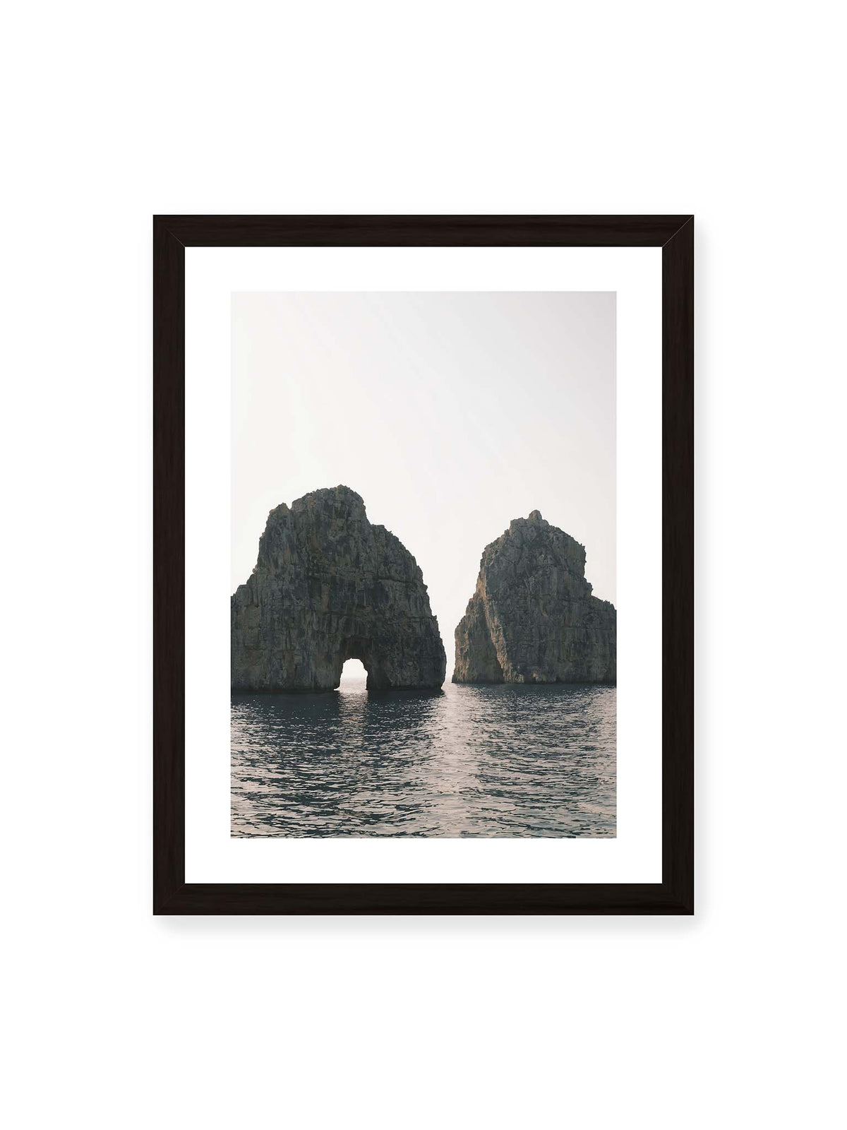 30x40 cm, weißer Galerie-Rand, schwarzer Rahmen – Zwei massive Felsformationen im Meer, eine mit natürlichem Felsbogen, vor hellem Himmel.