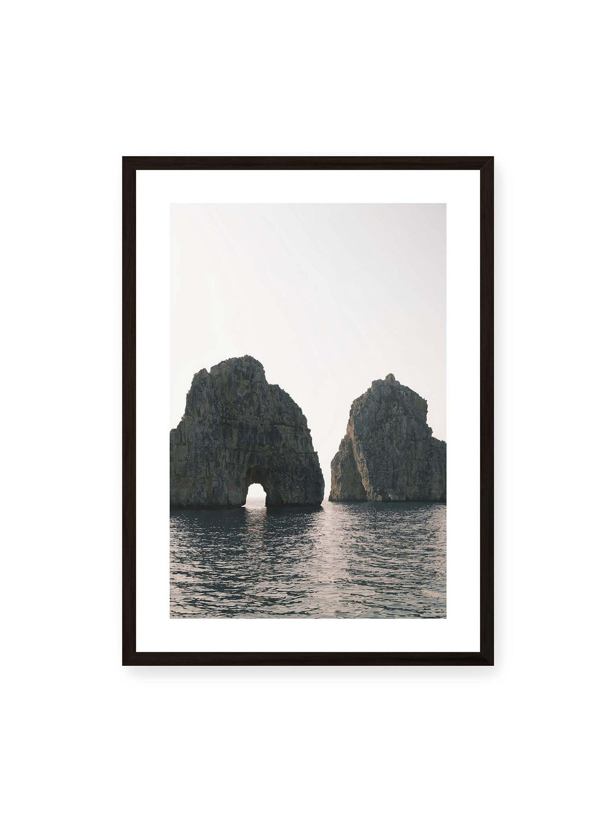 50x70 cm, weißer Galerie-Rand, schwarzer Rahmen – Zwei massive Felsformationen im Meer, eine mit natürlichem Felsbogen, vor hellem Himmel.