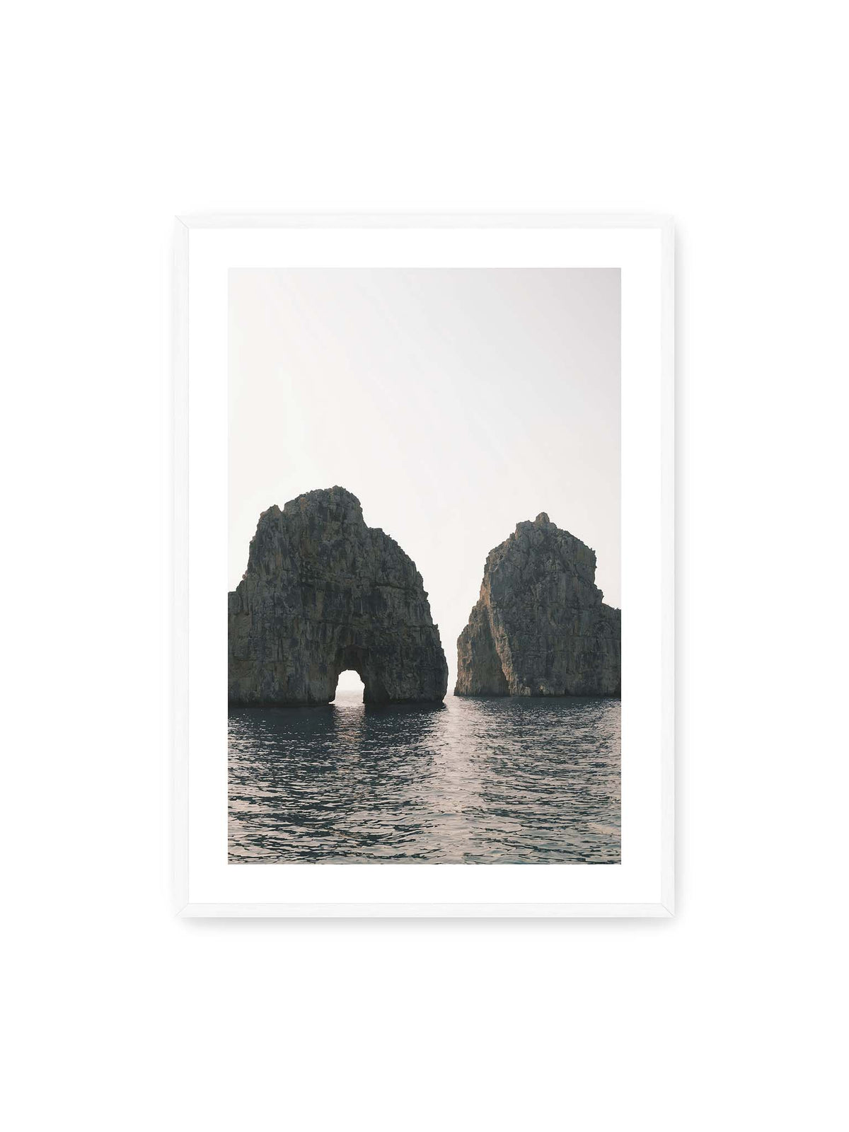70x100 cm, weißer Galerie-Rand, weißer Rahmen – Zwei massive Felsformationen im Meer, eine mit natürlichem Felsbogen, vor hellem Himmel.