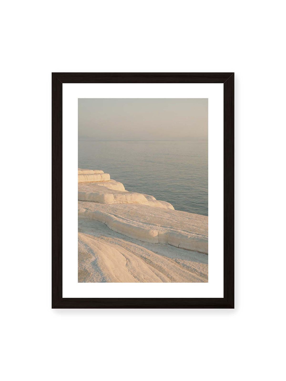 30x40 cm, weißer Galerie-Rand, schwarzer Rahmen – Helle terrassenartige Gesteinsflächen fallen in sanften Stufen zu einem ruhigen, blassblauen Meer ab.
