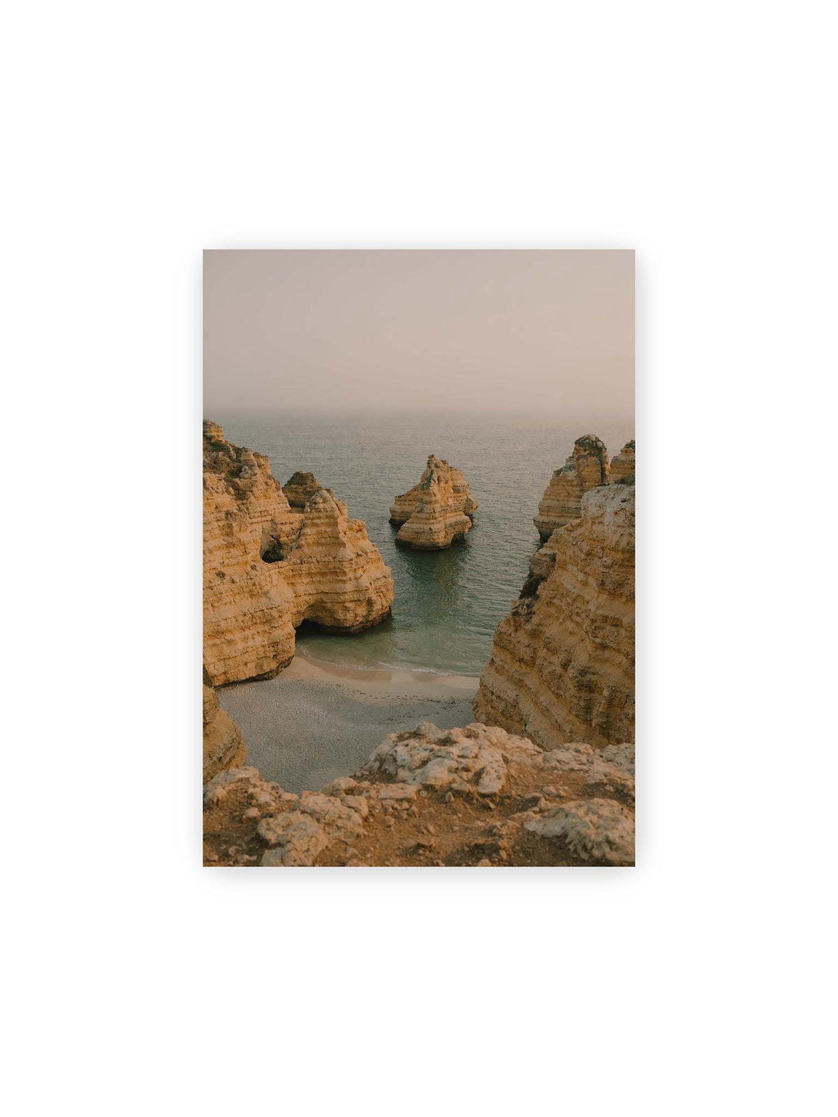 21x30 cm – Schichtartige Felsformationen umgeben eine kleine Bucht mit ruhigem Wasser und schmalem Sandstrand.