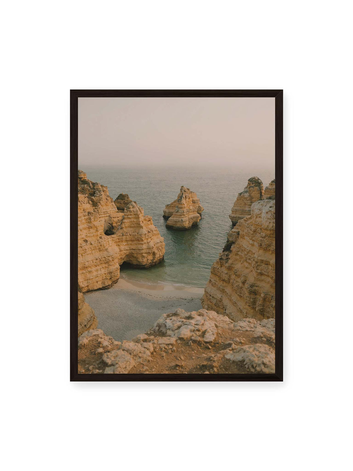 50x70 cm, schwarzer Rahmen – Schichtartige Felsformationen umgeben eine kleine Bucht mit ruhigem Wasser und schmalem Sandstrand.