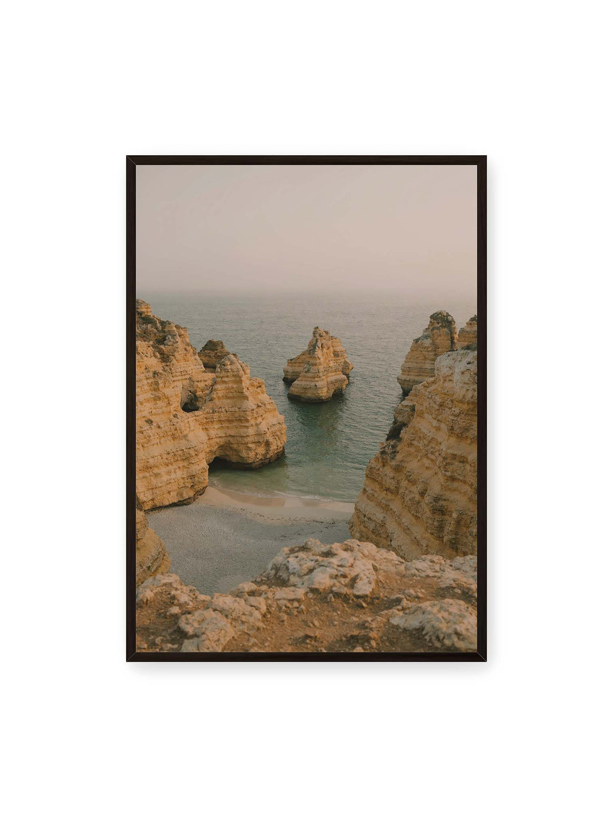 70x100 cm, schwarzer Rahmen – Schichtartige Felsformationen umgeben eine kleine Bucht mit ruhigem Wasser und schmalem Sandstrand.
