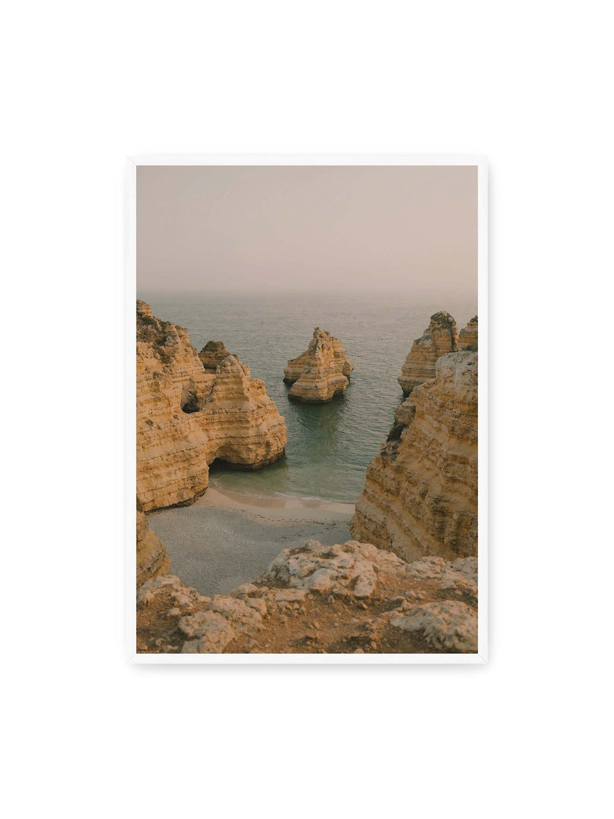 70x100 cm, weißer Rahmen – Schichtartige Felsformationen umgeben eine kleine Bucht mit ruhigem Wasser und schmalem Sandstrand.