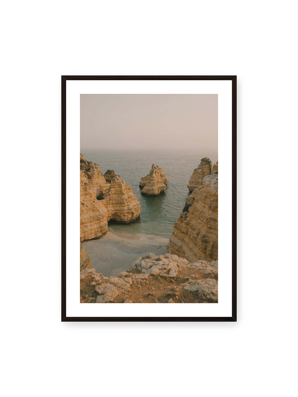 70x100 cm, weißer Galerie-Rand, schwarzer Rahmen – Schichtartige Felsformationen umgeben eine kleine Bucht mit ruhigem Wasser und schmalem Sandstrand.