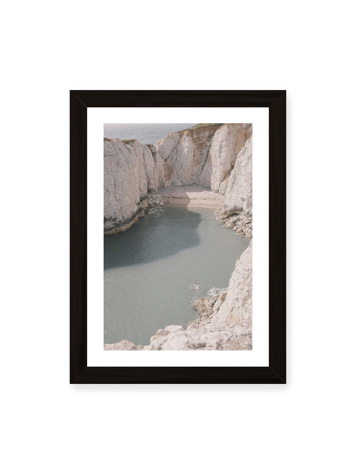 21x30 cm, weißer Galerie-Rand, schwarzer Rahmen – Helle steile Felswände umschließen eine kleine Bucht mit ruhigem Wasser und einem schmalen Strand.