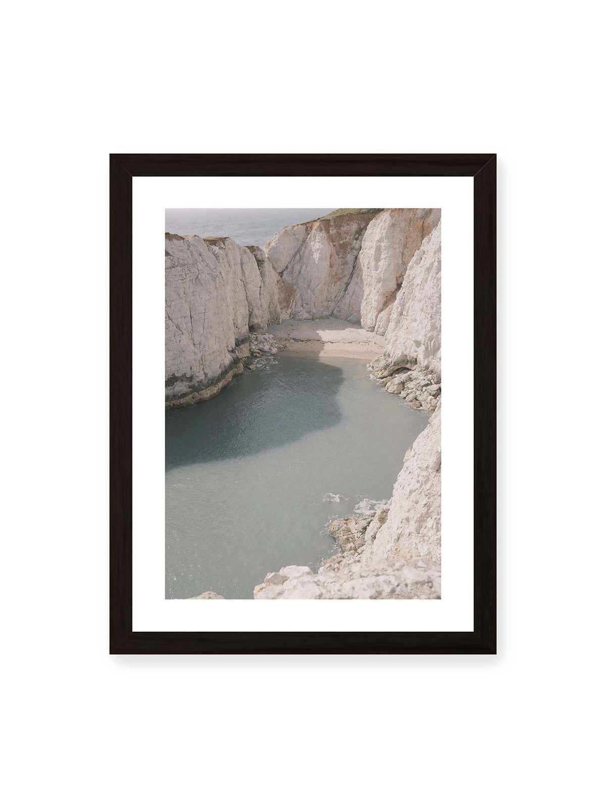 30x40 cm, weißer Galerie-Rand, schwarzer Rahmen – Helle steile Felswände umschließen eine kleine Bucht mit ruhigem Wasser und einem schmalen Strand.