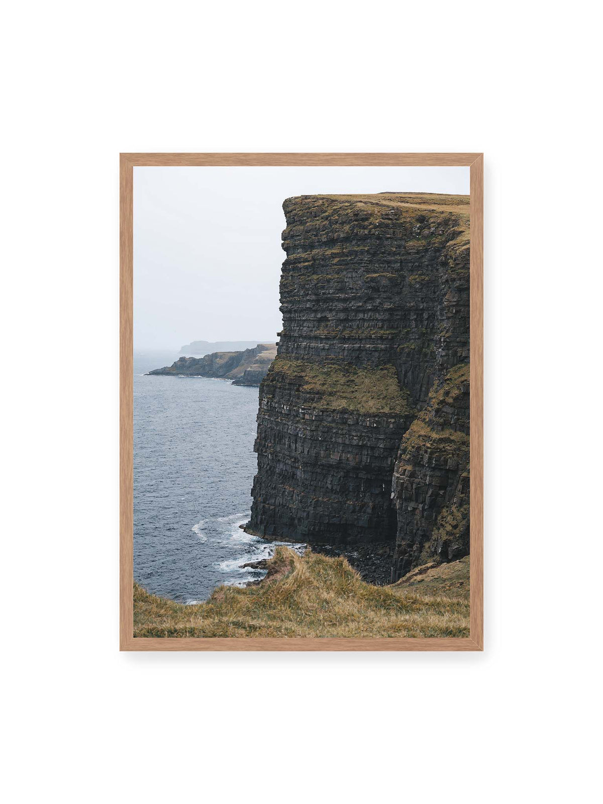 50x70 cm, Eichenrahmen – Dunkle geschichtete Klippen fallen steil zum Meer ab, während weitere Felswände in der hellen Ferne verschwinden.