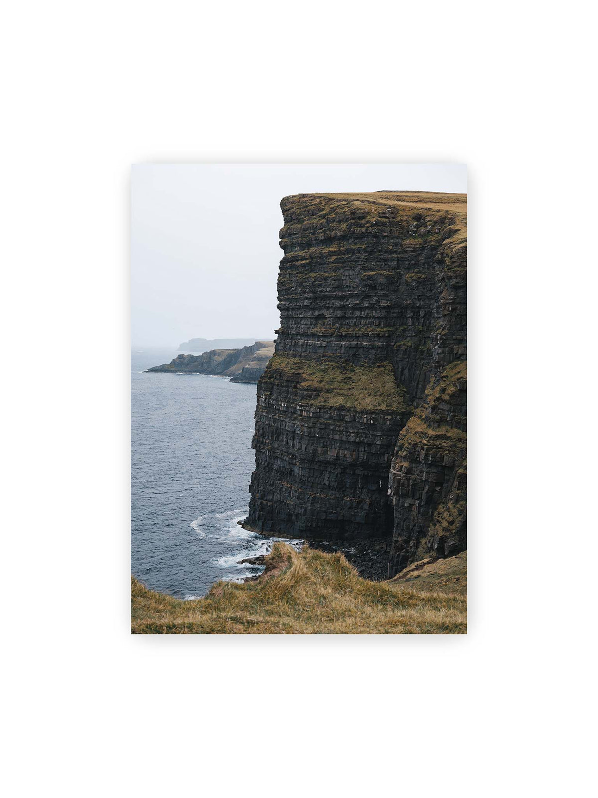 50x70 cm – Dunkle geschichtete Klippen fallen steil zum Meer ab, während weitere Felswände in der hellen Ferne verschwinden.