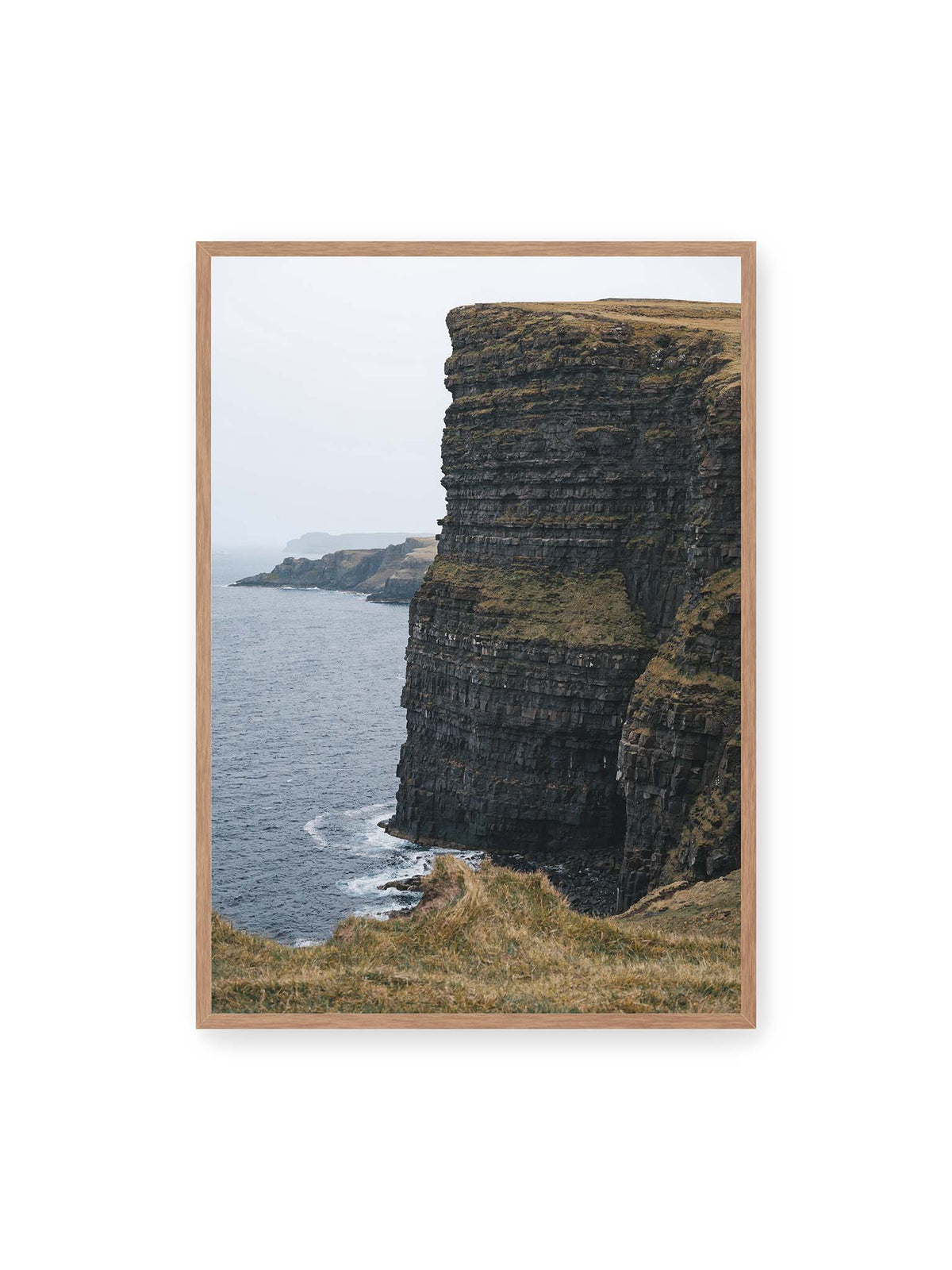 70x100 cm, Eichenrahmen – Dunkle geschichtete Klippen fallen steil zum Meer ab, während weitere Felswände in der hellen Ferne verschwinden.